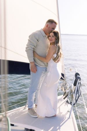 Couple embracing on sailboat deck with white sail and open water in background.