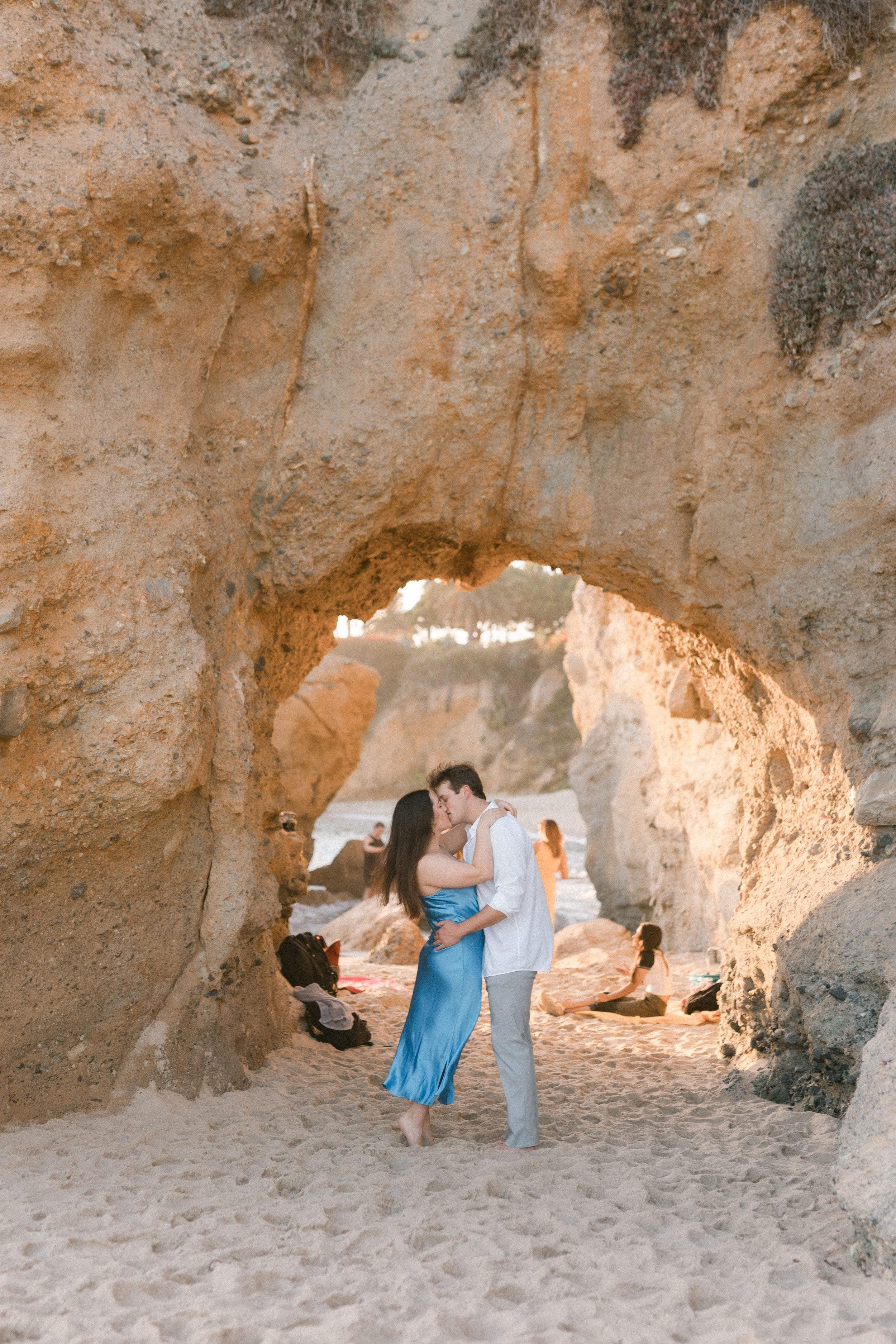 Romantic couple embracing under natural rock arch on sandy beach at golden hour.