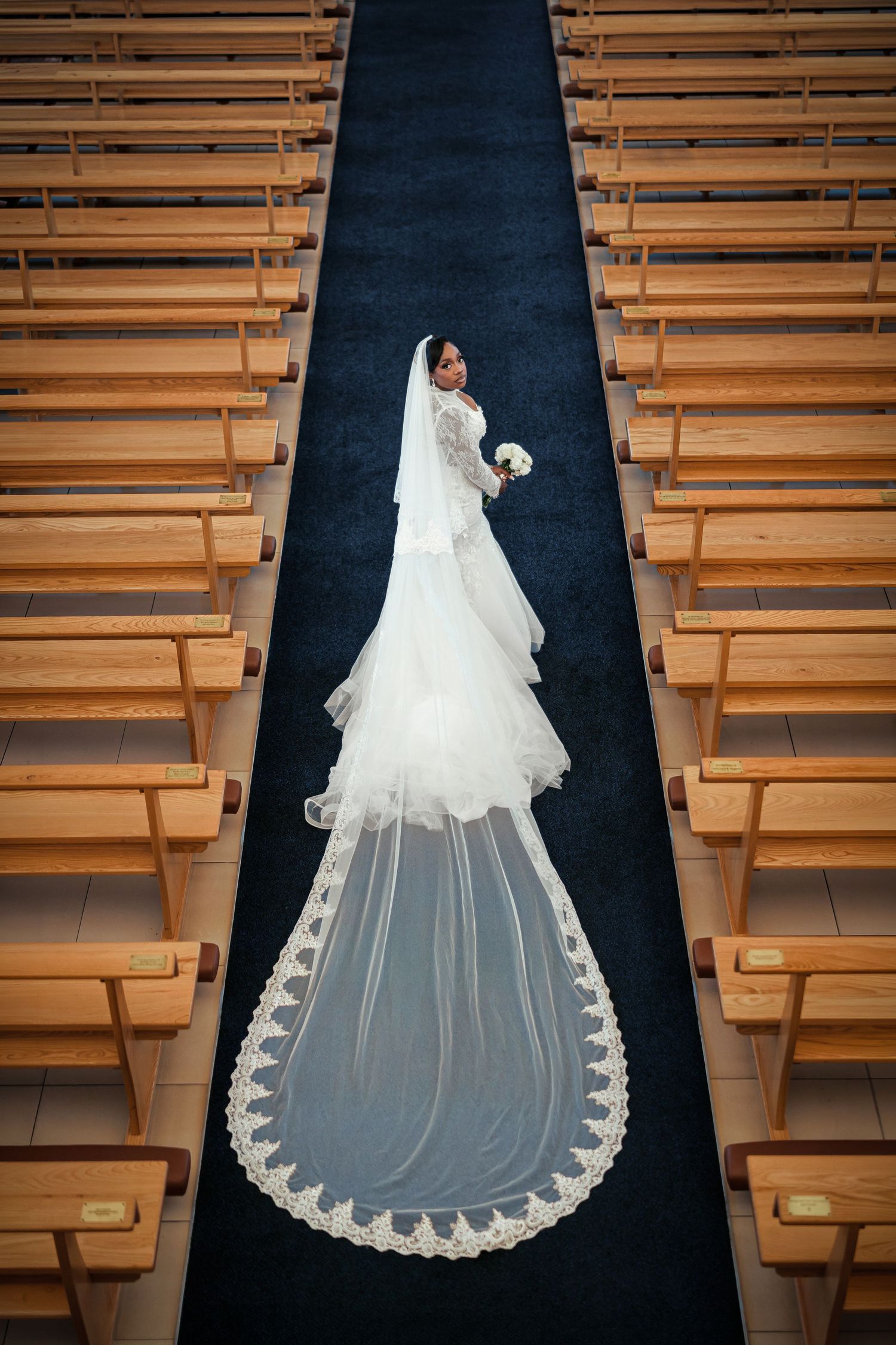 A bride with a radiant smile glances through her delicate white veil in soft natural lighting.