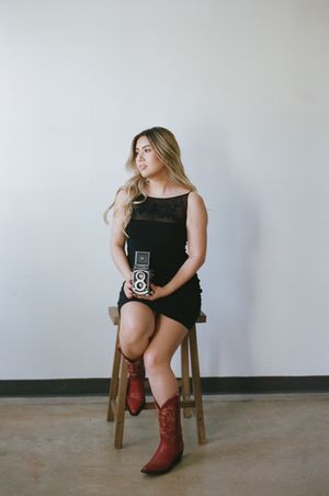 Studio portrait with vintage camera and red cowboy boots against white background.