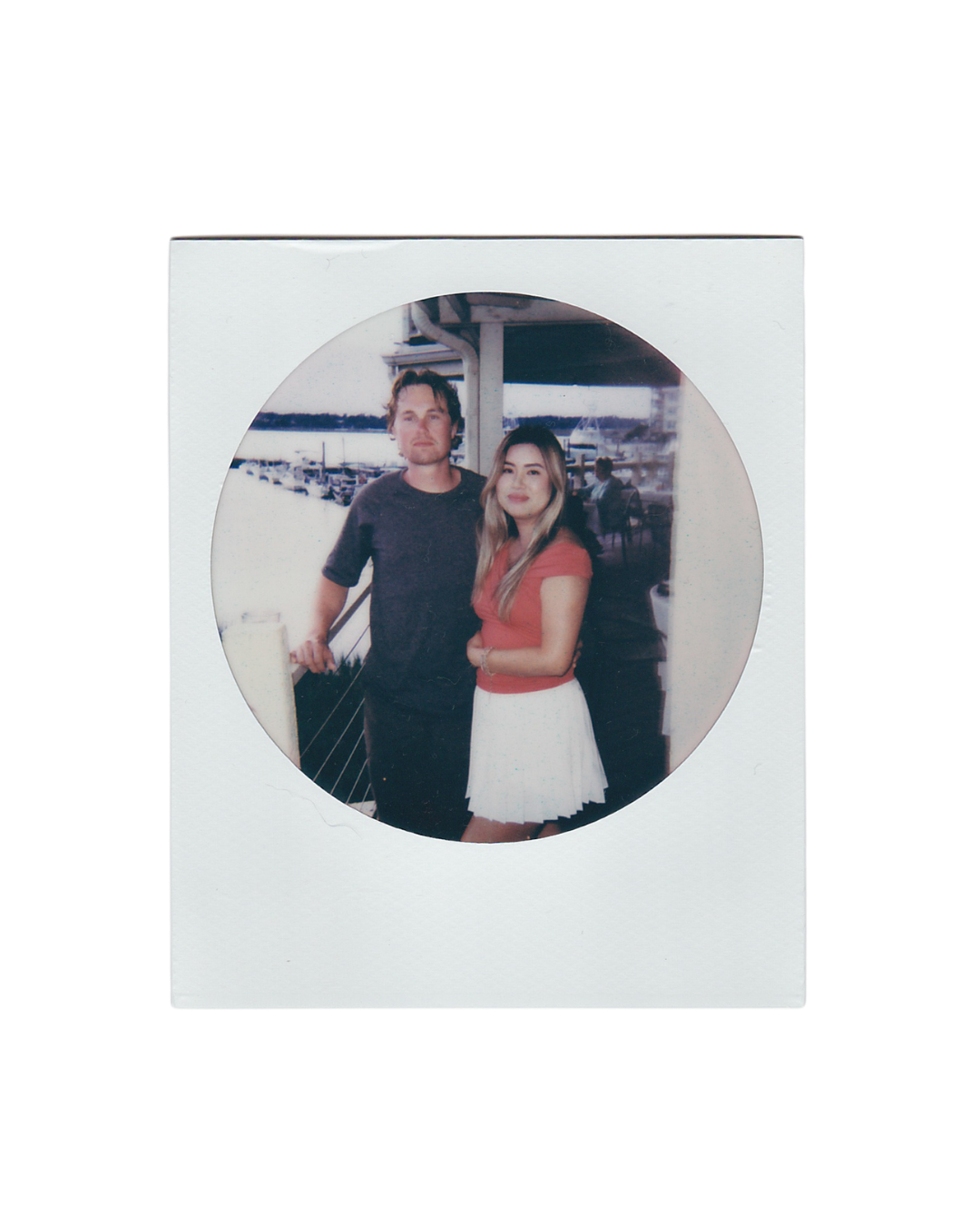 Couple posing together in a circular Instax photo frame, man in black shirt and woman in red top and white skirt.