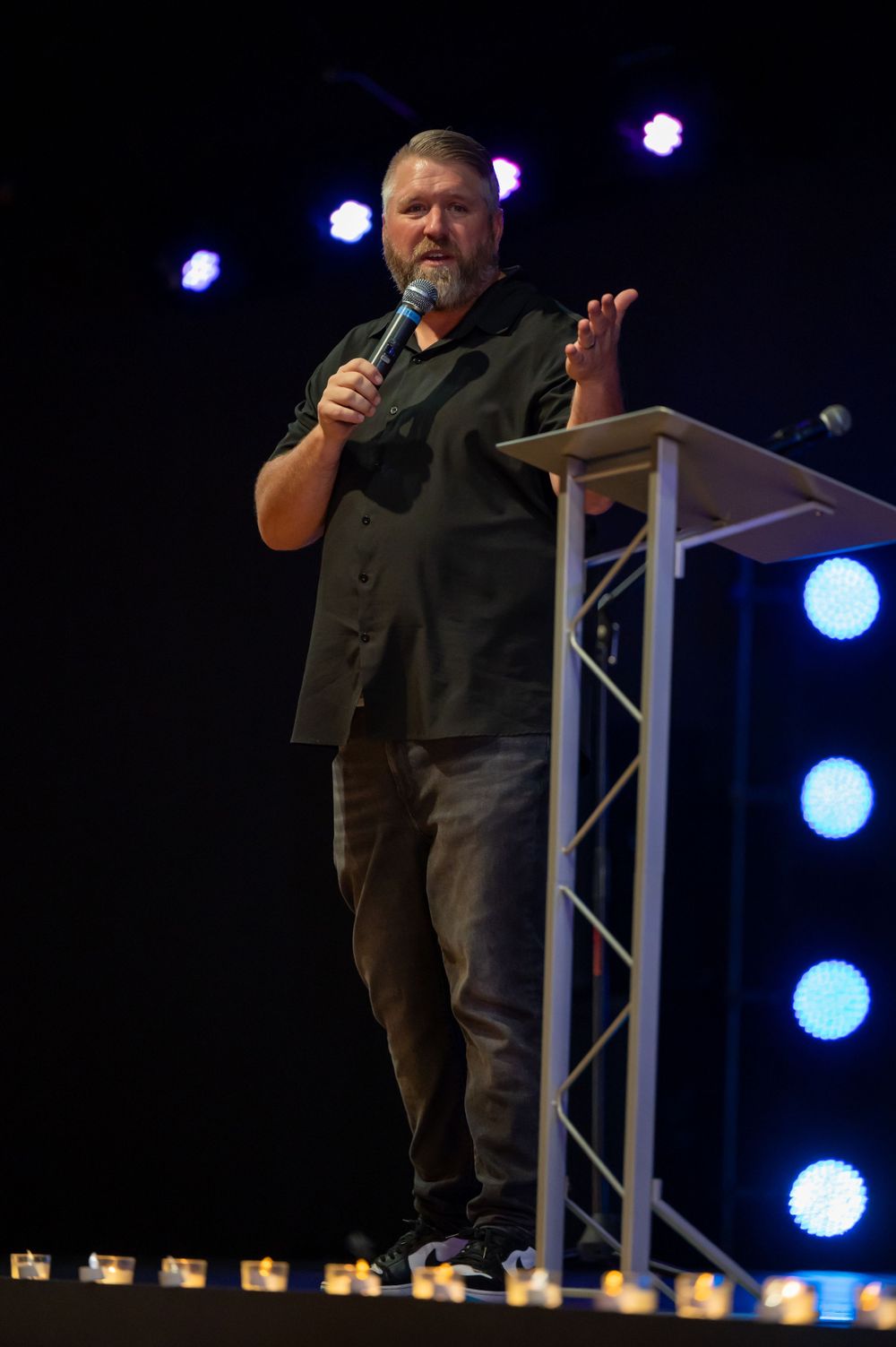 A speaker stands on an elevated platform with dramatic blue spotlighting.
