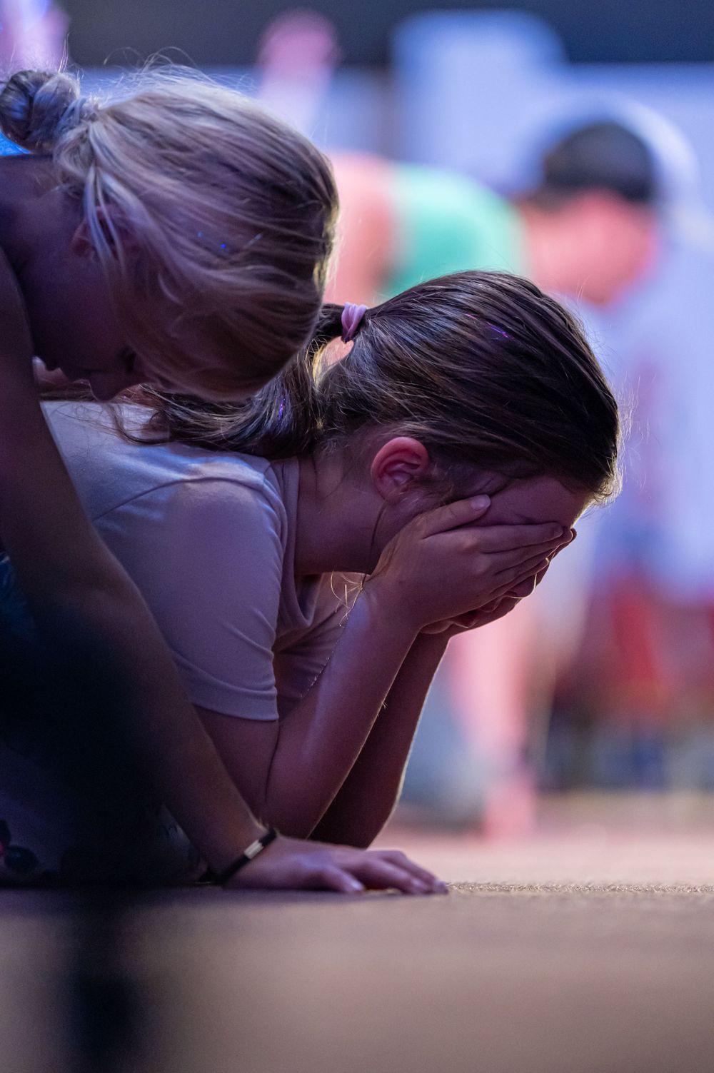 Two people kneel in prayer during an emotional moment at an event.
