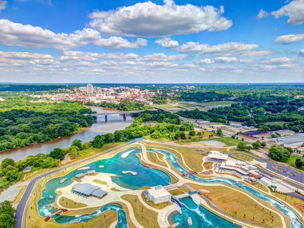 Aerial view of a city skyline with a river and vibrant aqua-colored water park in the foreground.