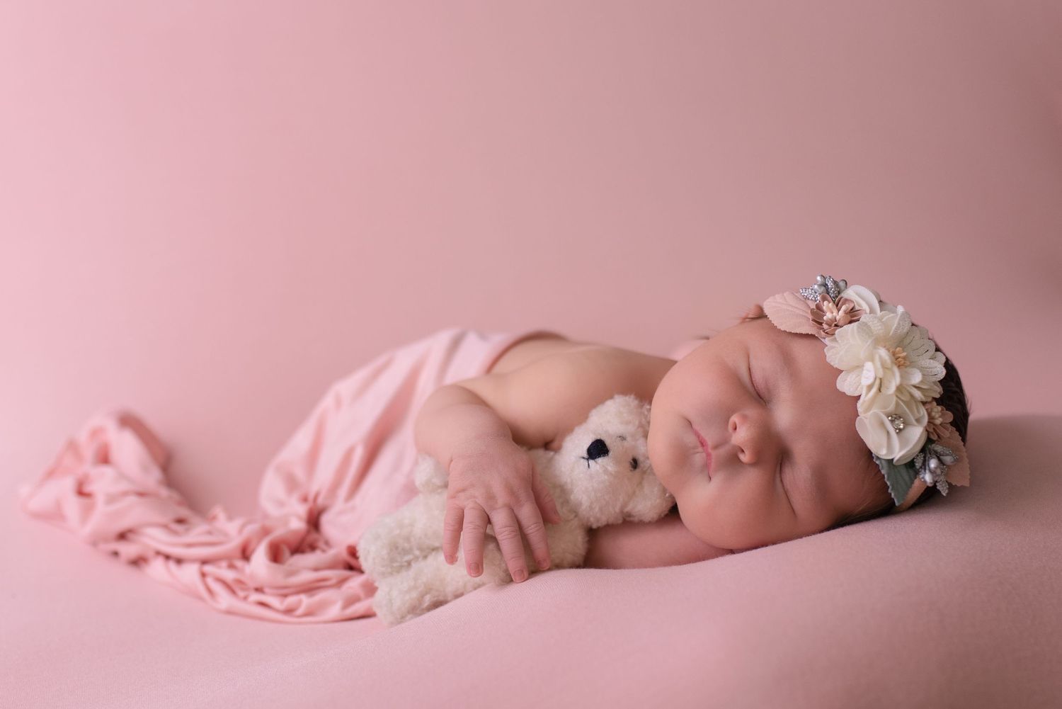 Minimalist newborn photography setup with soft pink backdrop and white accessories.