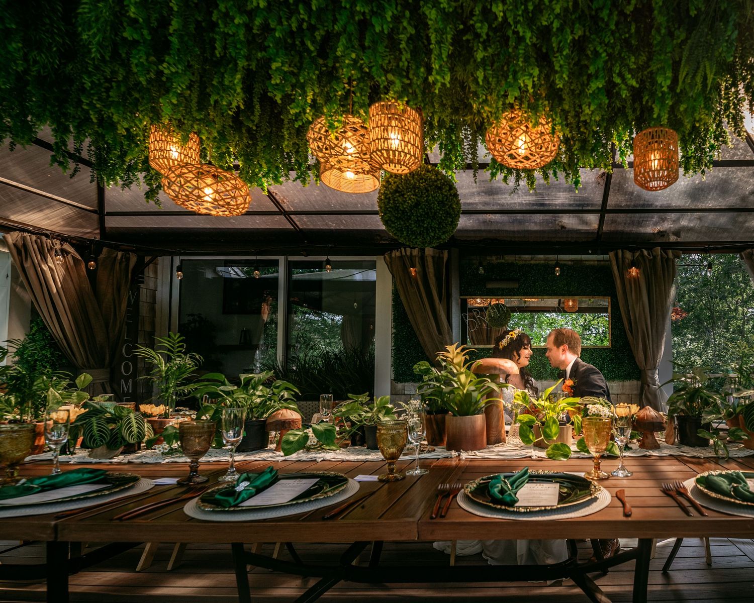 Rustic wedding reception table setup with hanging lights and greenery overhead.