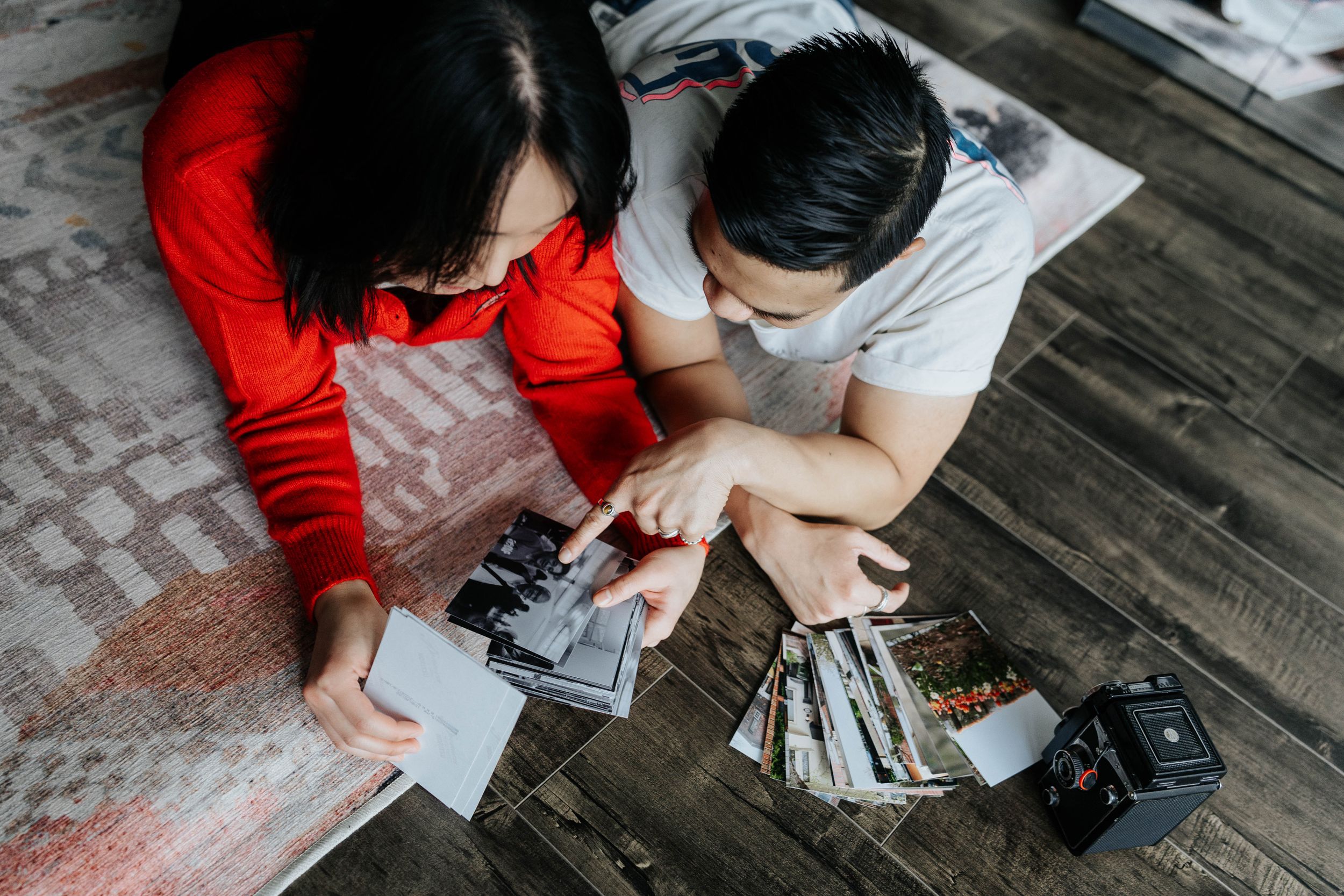 Two people looking through photographs together on a wooden floor.