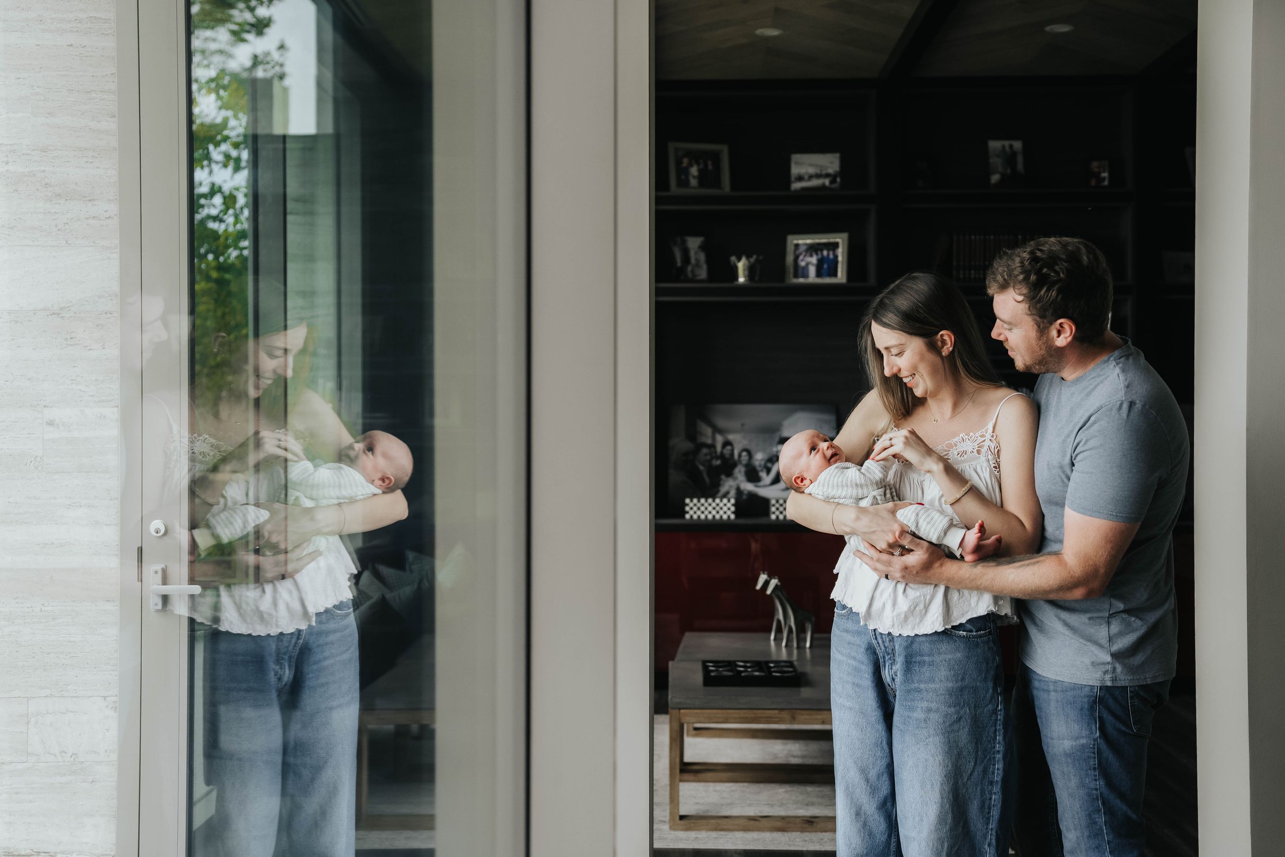 A couple stands in front of large windows in a cozy home setting, sharing an intimate embrace.