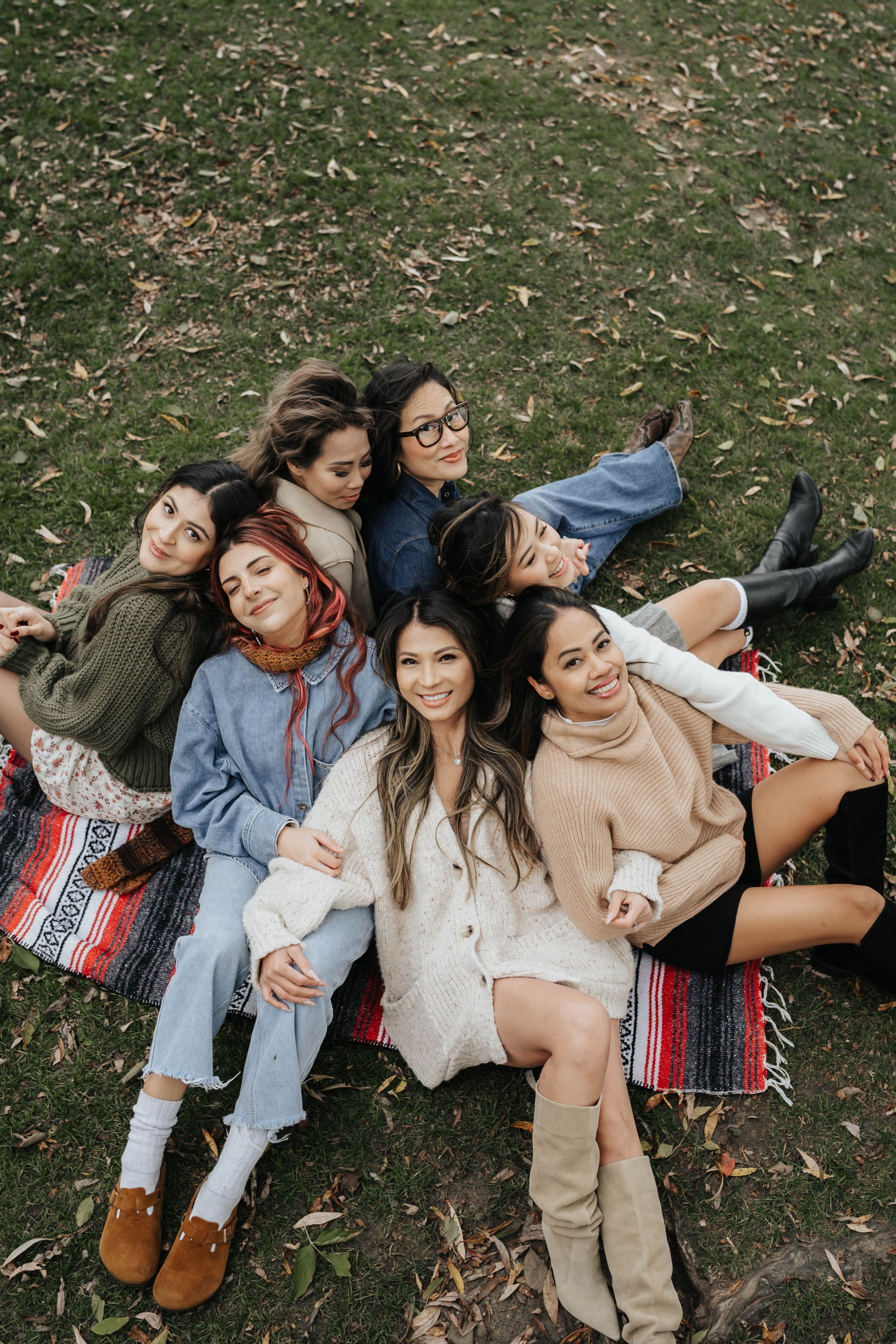 A group of friends lying on grass in casual autumn outfits creating a playful candid photo series.