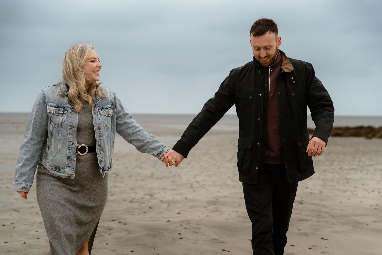 Couple walking and laughing together on cloudy beach.