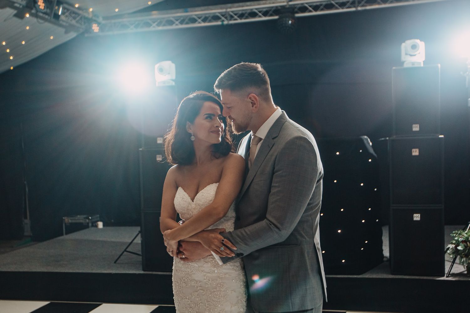 Romantic couple embraces on dimly lit dance floor during intimate wedding moment.
