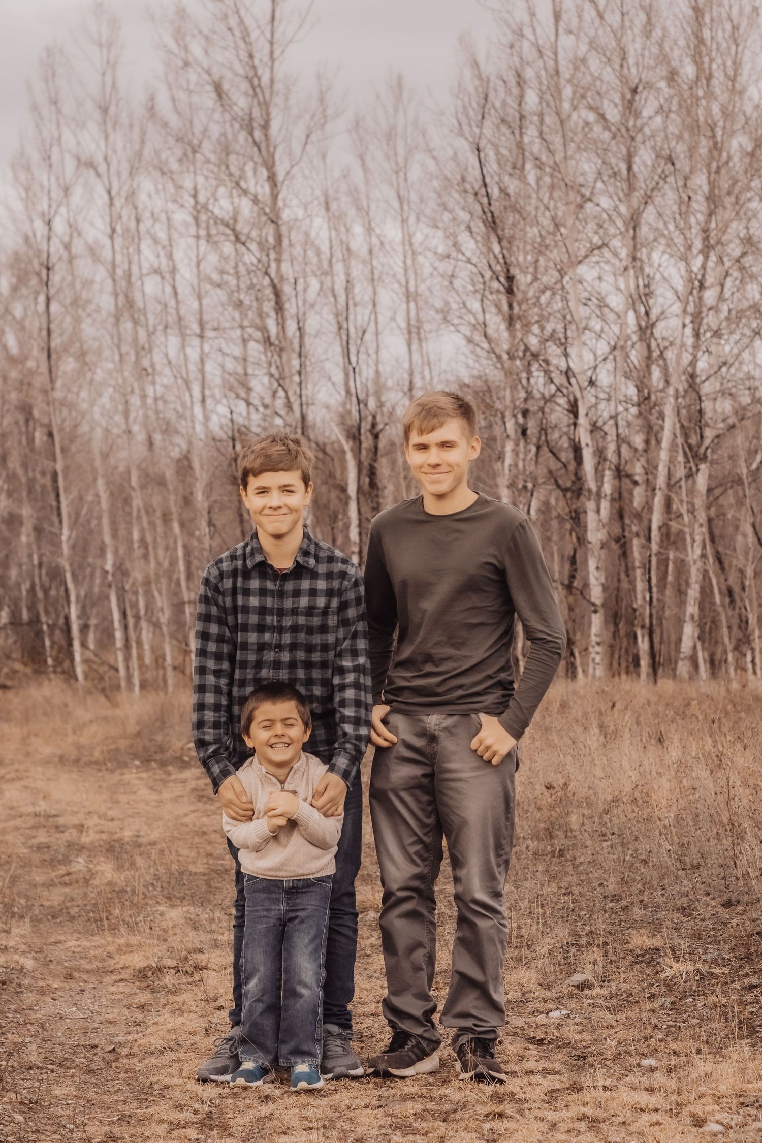 Three siblings standing together outdoors against bare autumn trees.