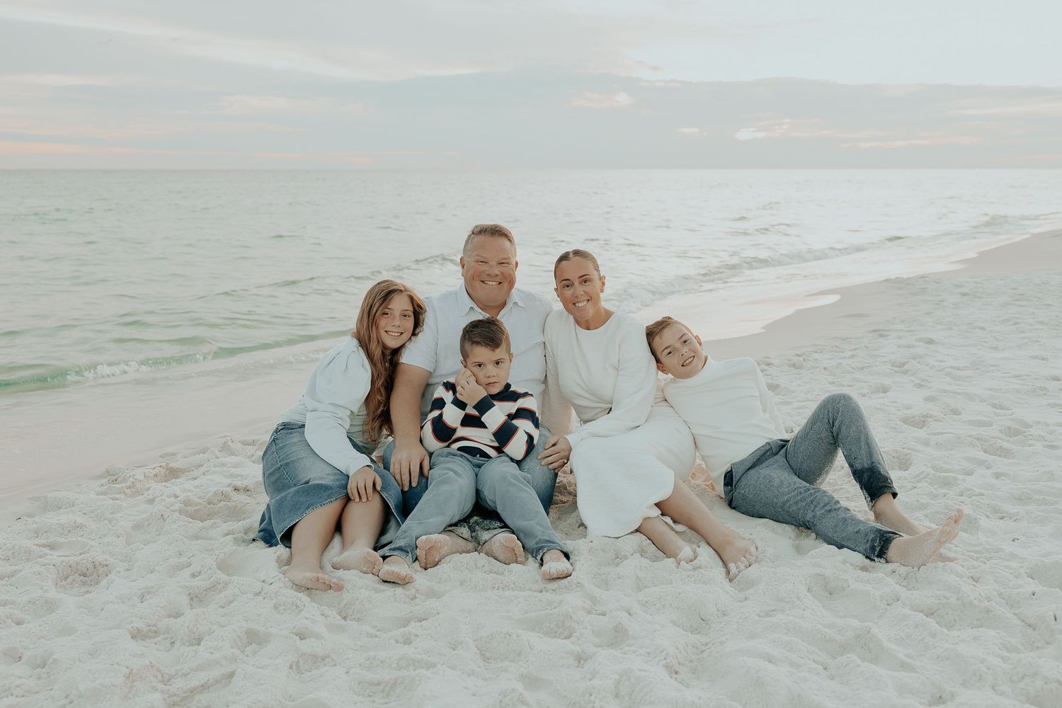 Family relaxing together on sandy beach during sunset photoshoot.
