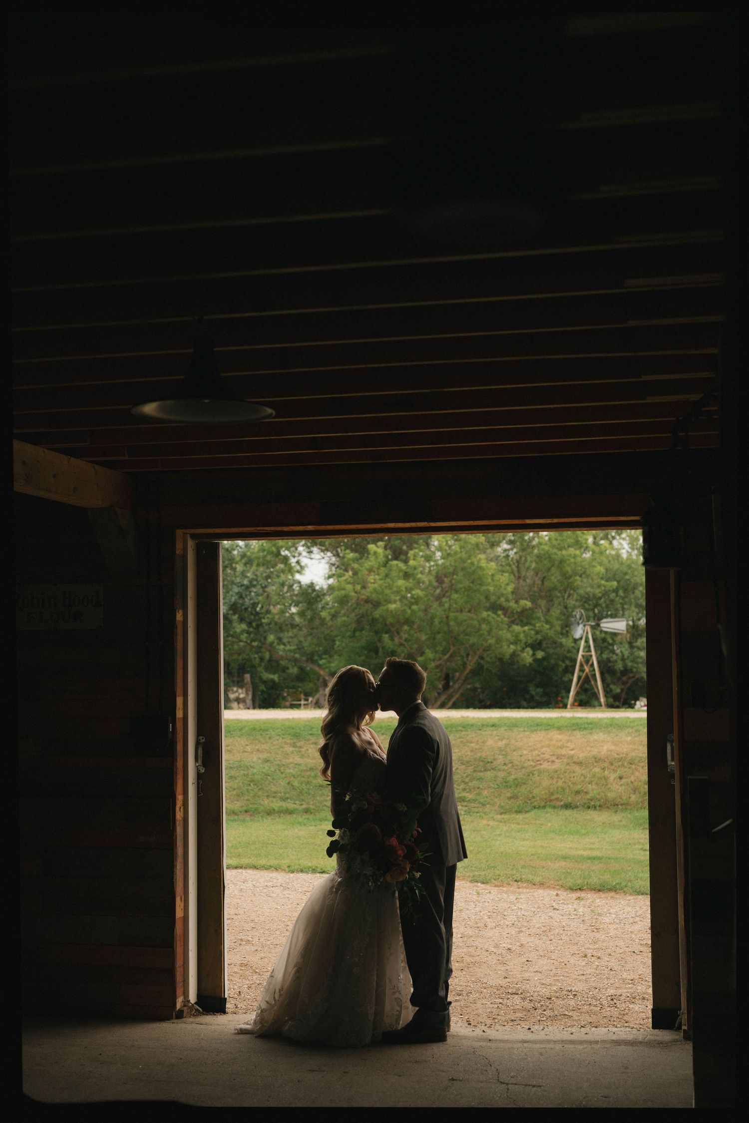 A silhouetted couple stands in a rustic barn doorway overlooking a green lawn with a swing set visible in the distance.
Saskatoon Wedding