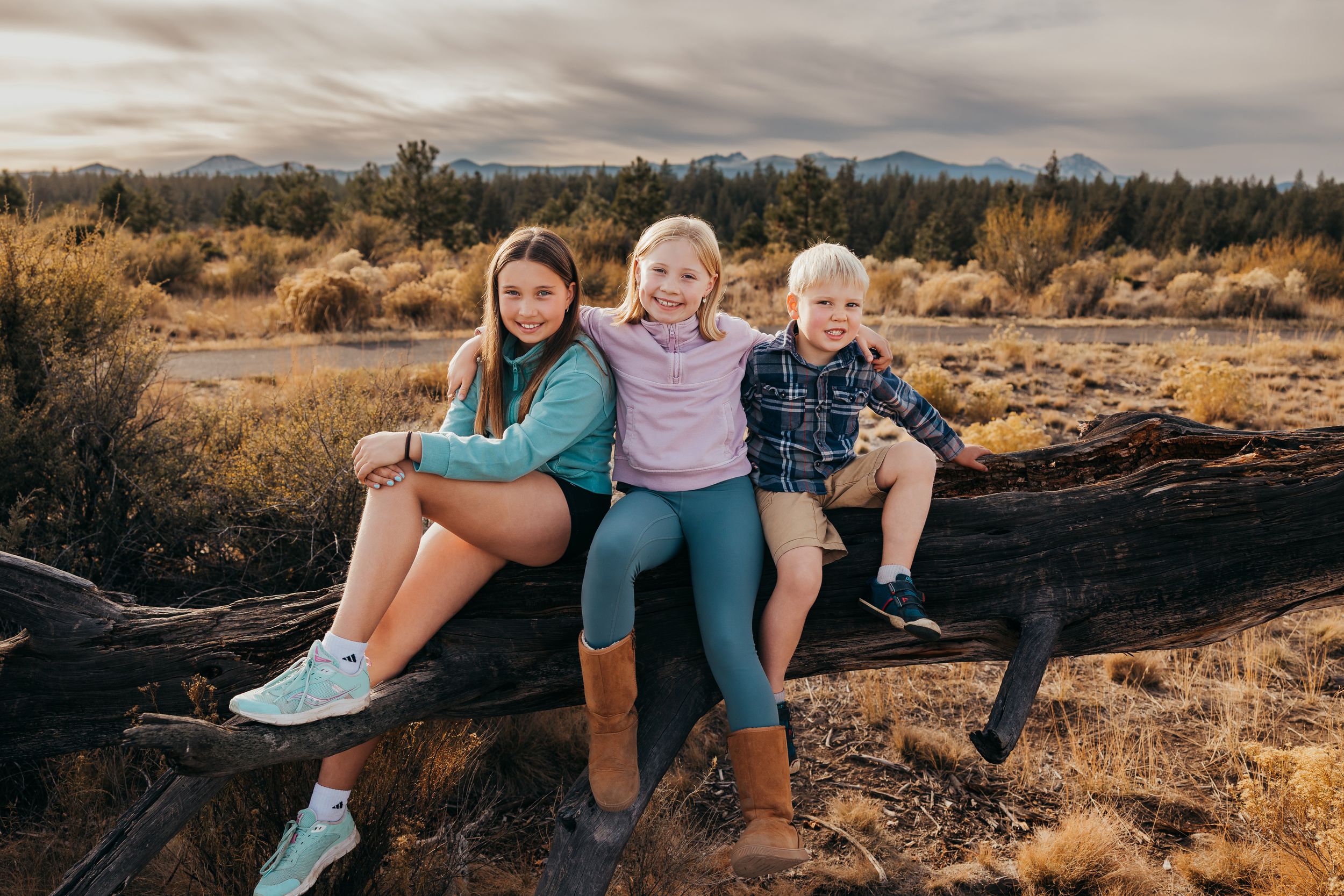 A group sits together on a fallen log at sunset in a desert landscape with mountains in the background.