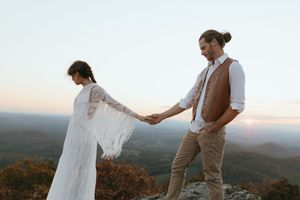 A couple stands together on a mountain overlook during sunset, surrounded by scenic autumn views and rolling hills.
