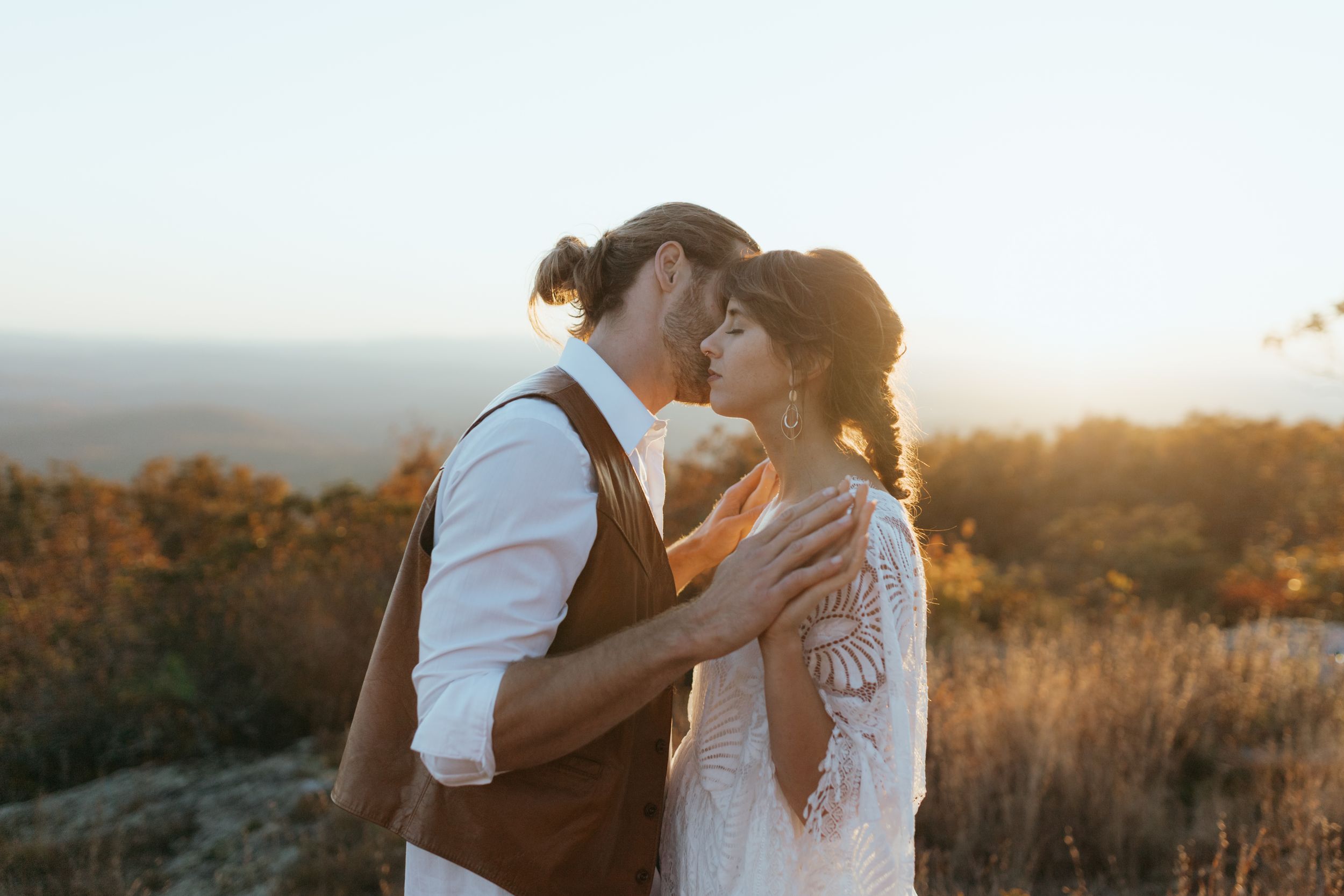 Couple embraces in golden sunlight during outdoor sunset photoshoot in rustic field.