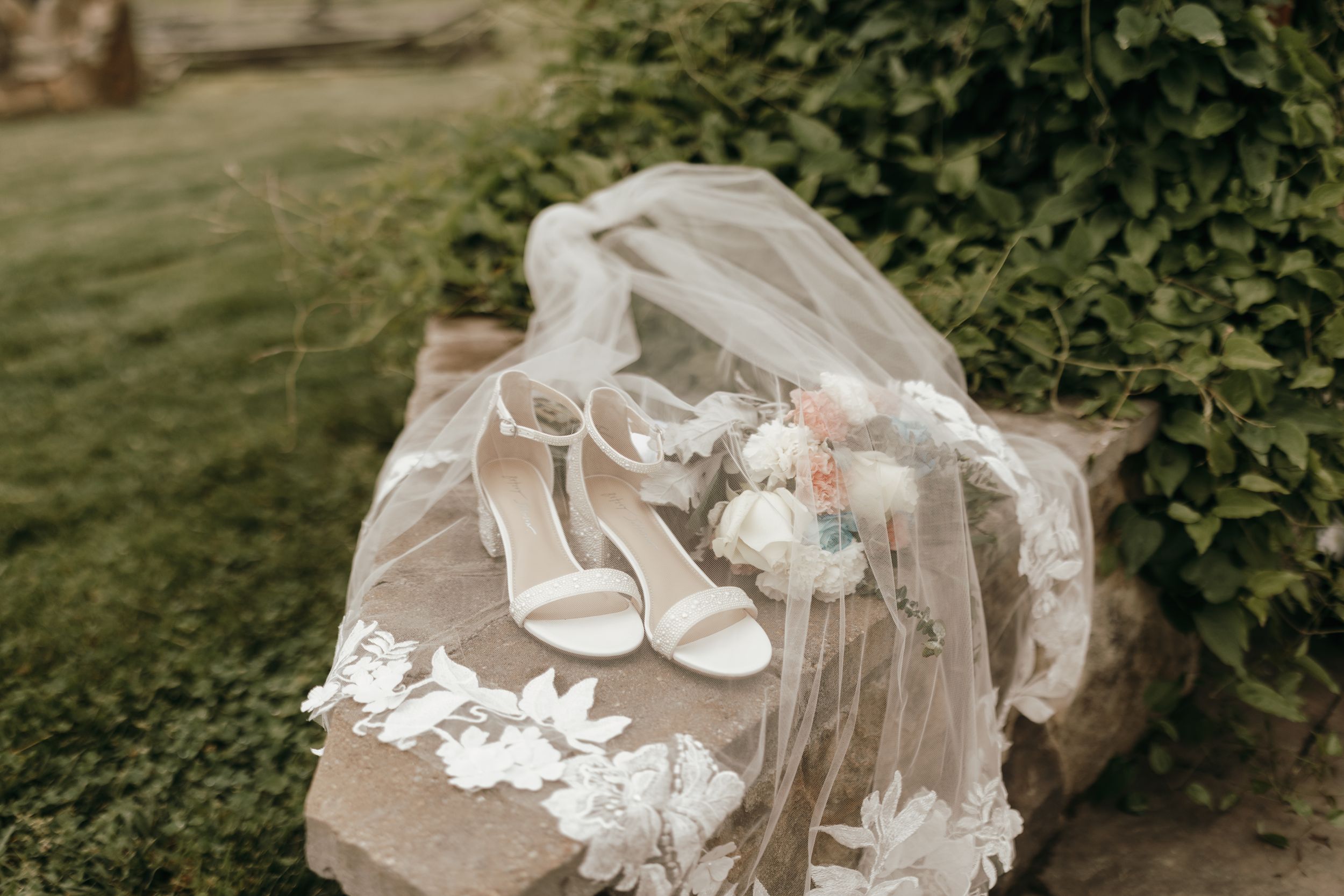 Wedding accessories including white heels and delicate lace veil arranged on rustic wood.