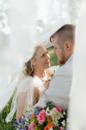 A romantic wedding moment captured through delicate lace veil with vibrant colorful bouquet in the foreground.