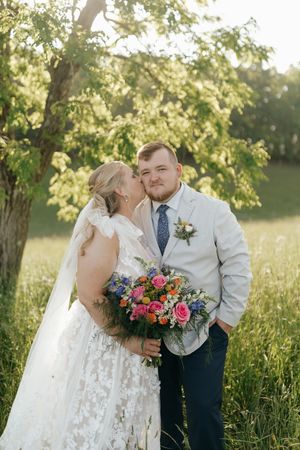 A couple shares romantic moments in a sun-dappled meadow with vibrant floral bouquet and wedding attire.