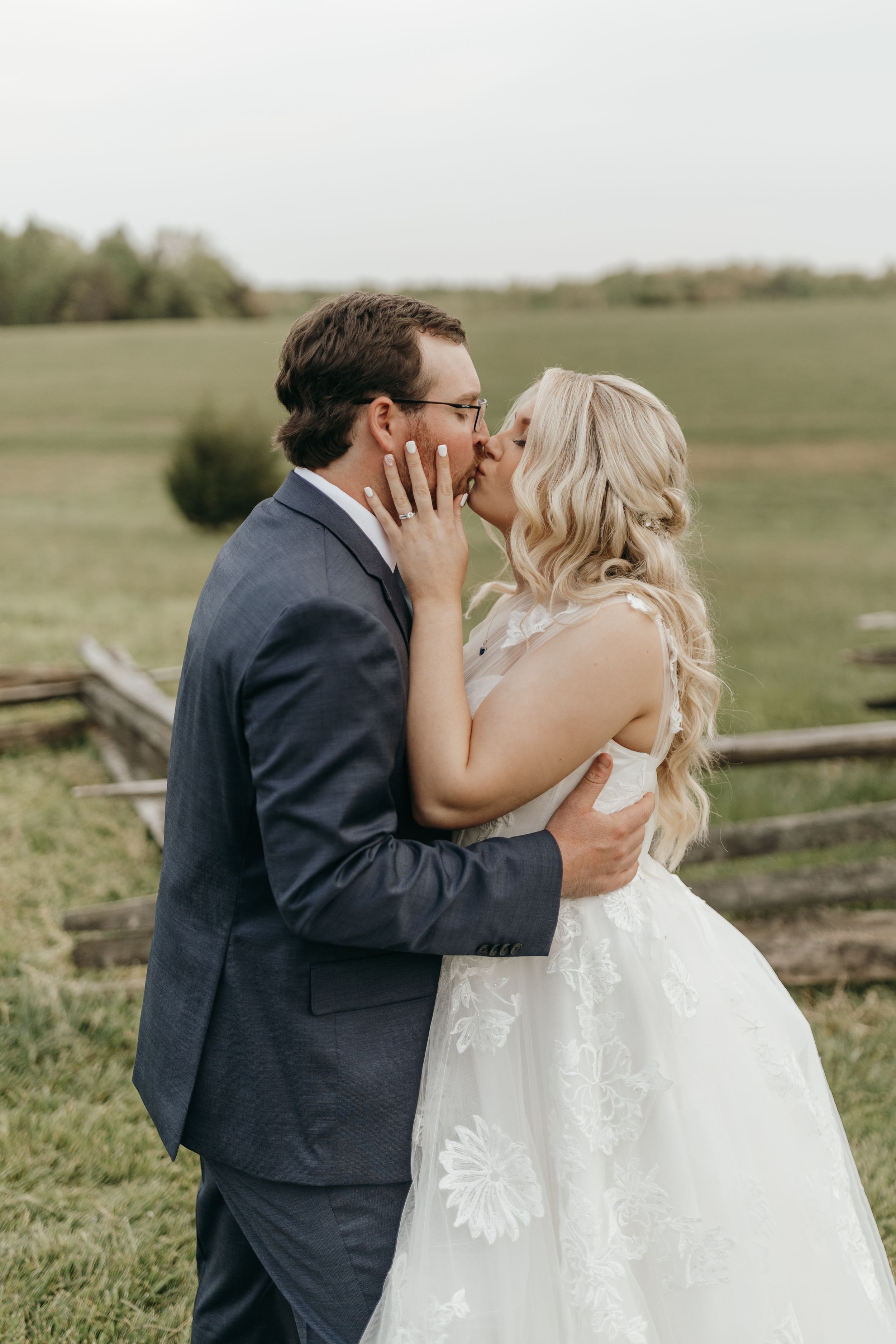 Intimate wedding moment captured between newlyweds near rustic wooden fence.