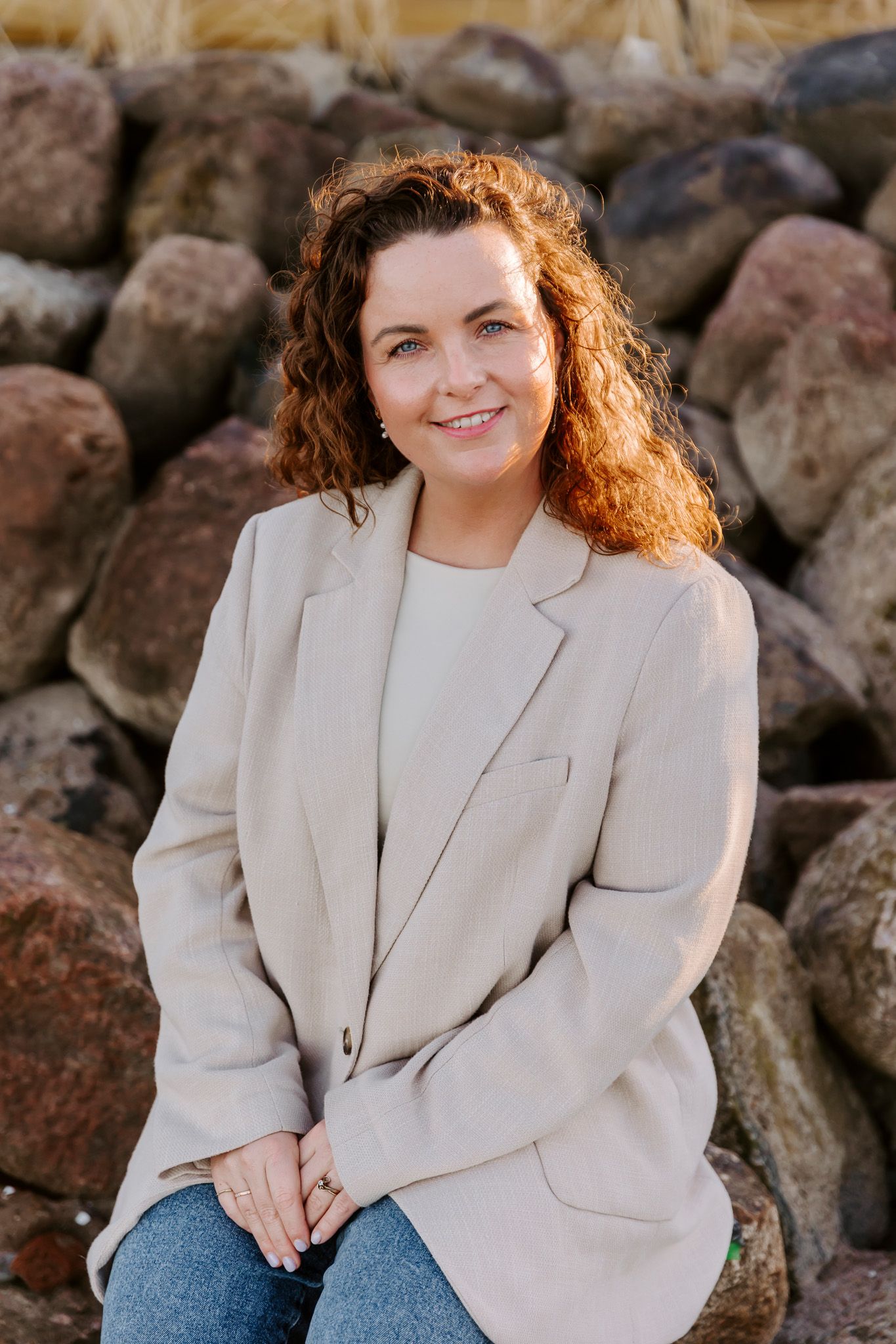 Professionel udendørs portrætsession med en cremefarvet blazer foran en klippefyldt, naturlig baggrund. Branding fotograf Fyn.