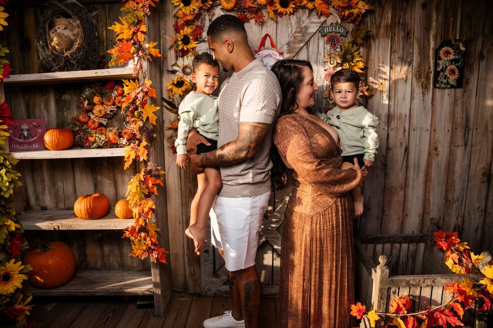 Family autumn portrait with rustic wooden backdrop decorated with pumpkins and fall foliage.