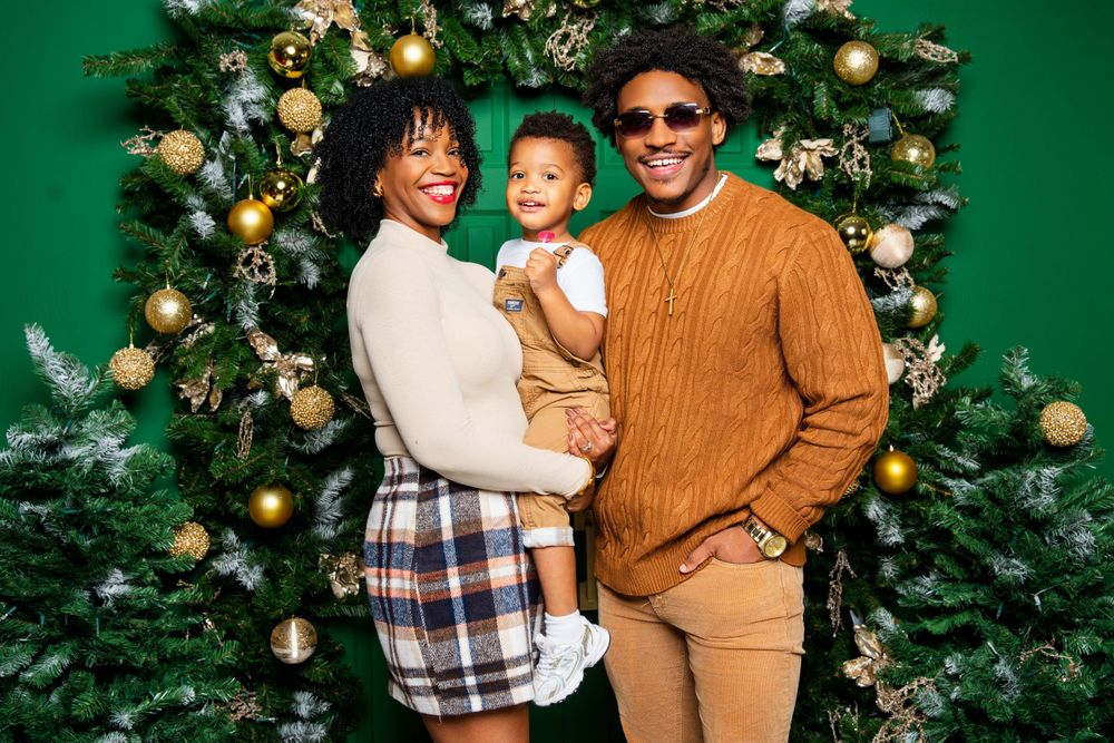 Holiday family portrait with decorated Christmas tree against green background.