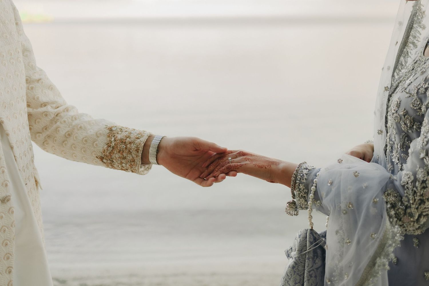 Close-up of bride and groom holding hands in traditional wedding attire.