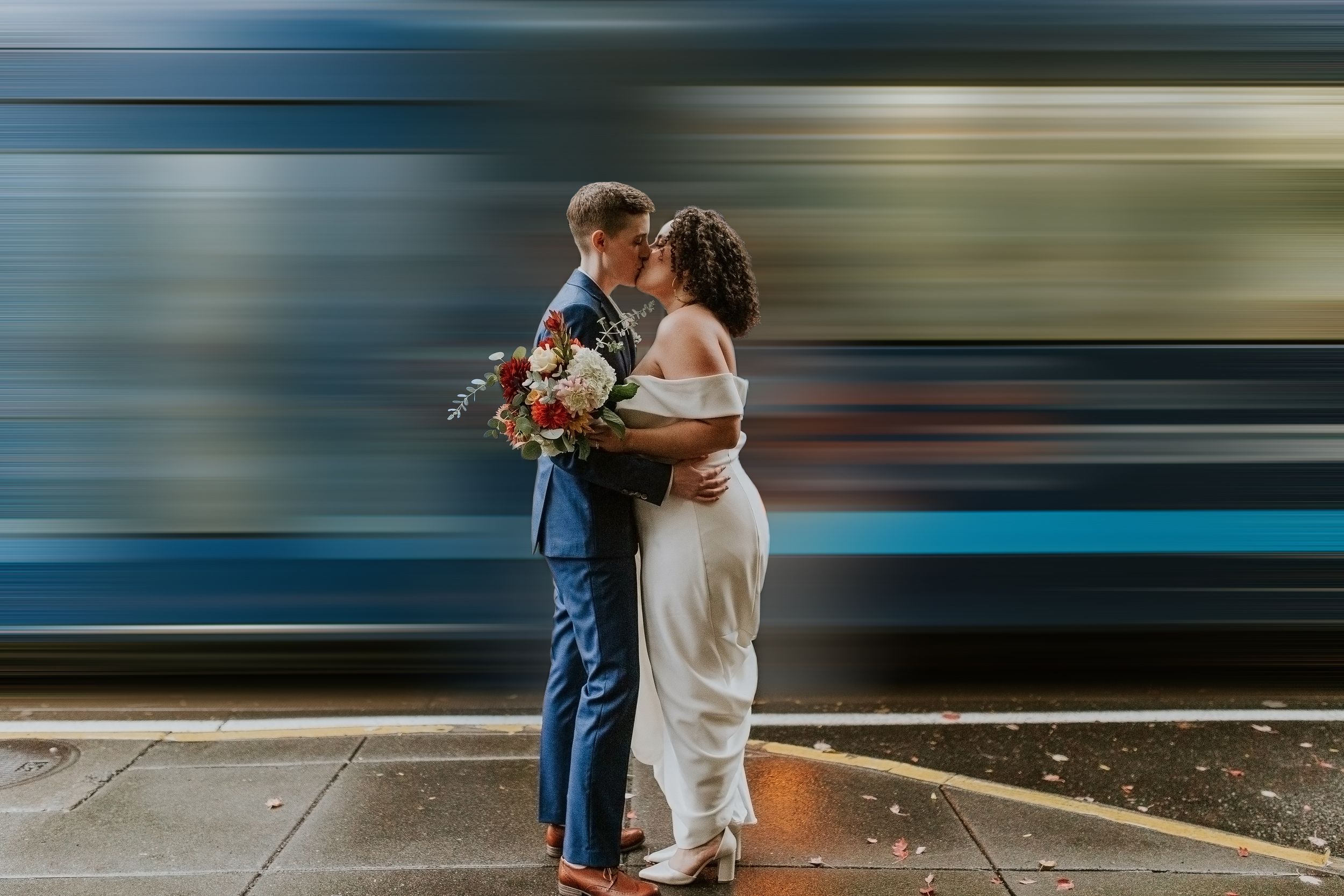 Couple embraces on train platform with motion-blurred subway car passing in background.  in Portland Or. Oregon wedding photographer.