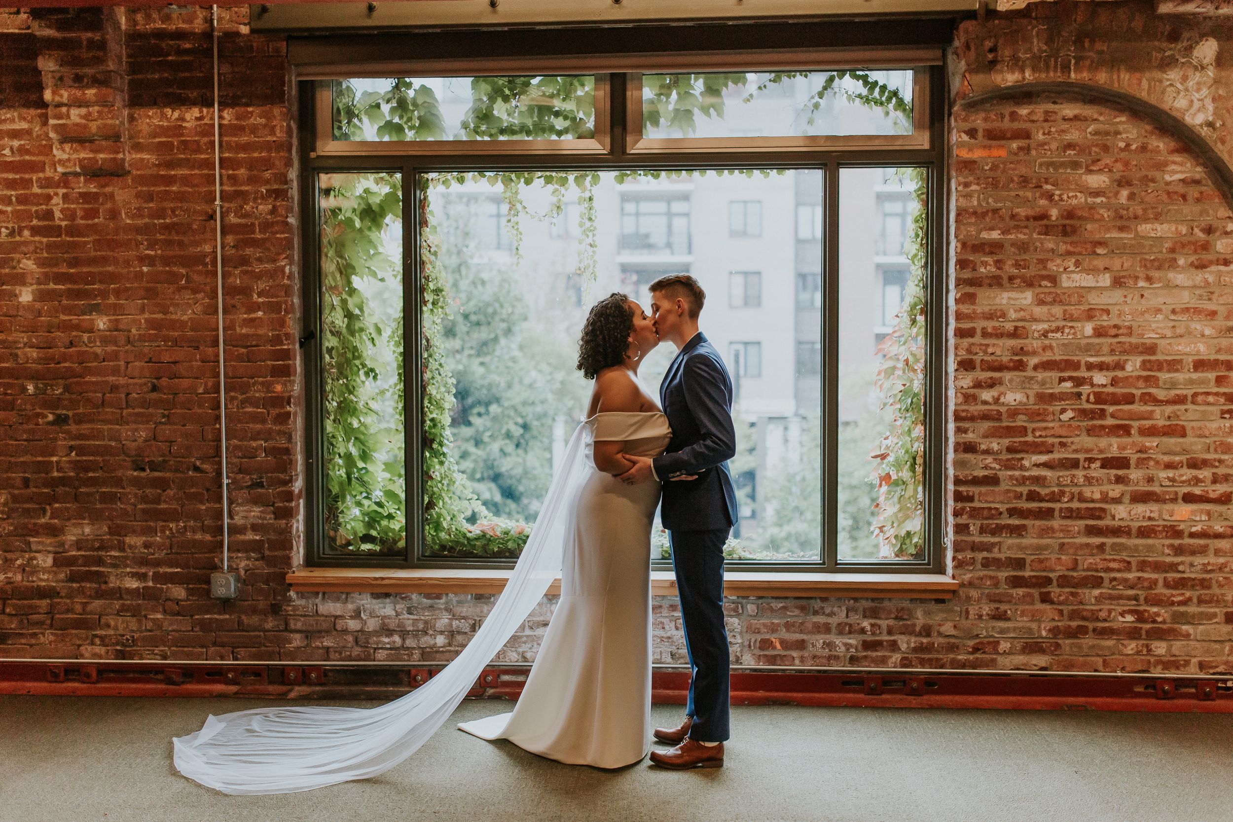 Elegant wedding moment in front of large window in rustic brick industrial space in Portland, Oregon. Portland Oregon wedding photography.
