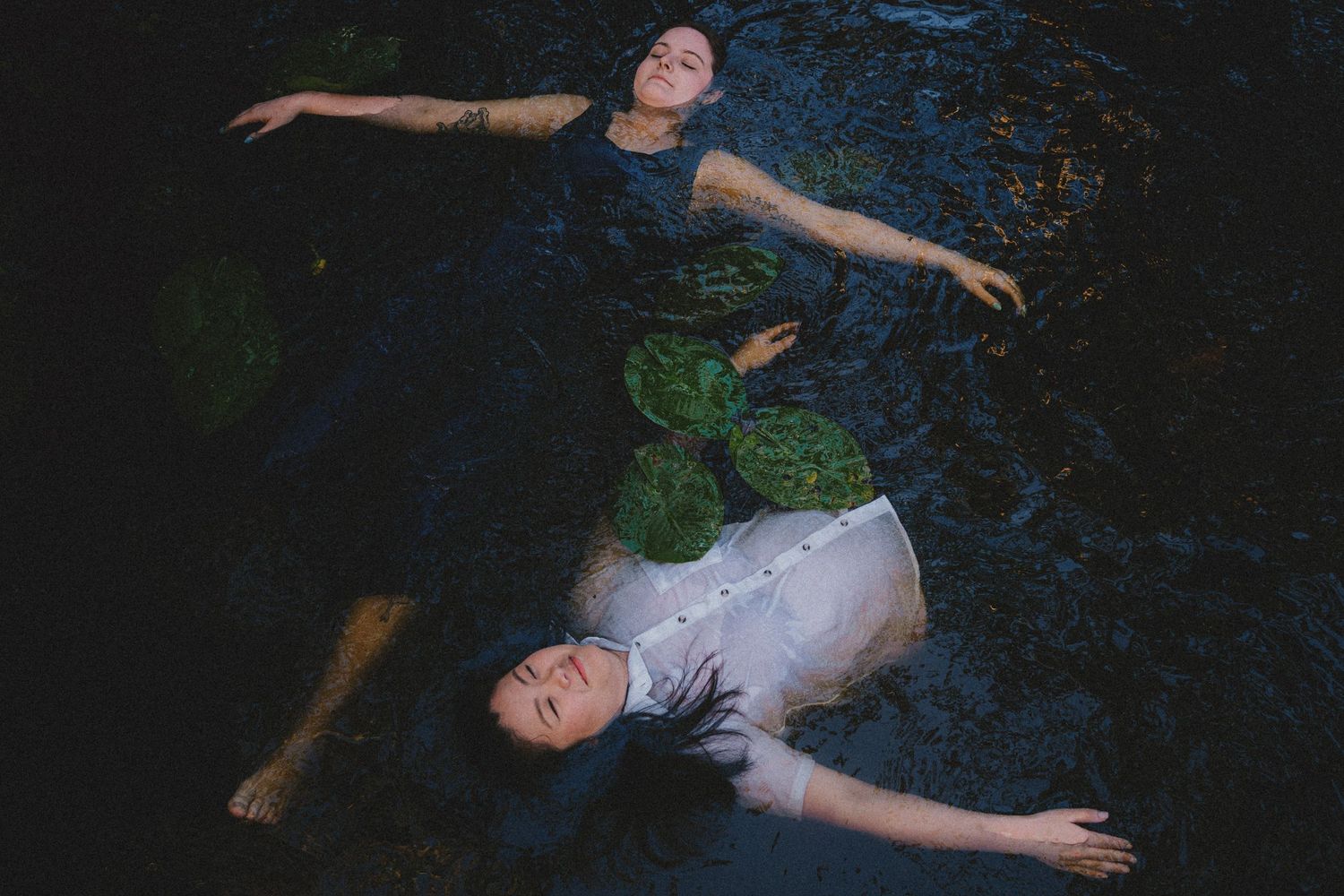 A couple floats peacefully in dark water, photographed from above.