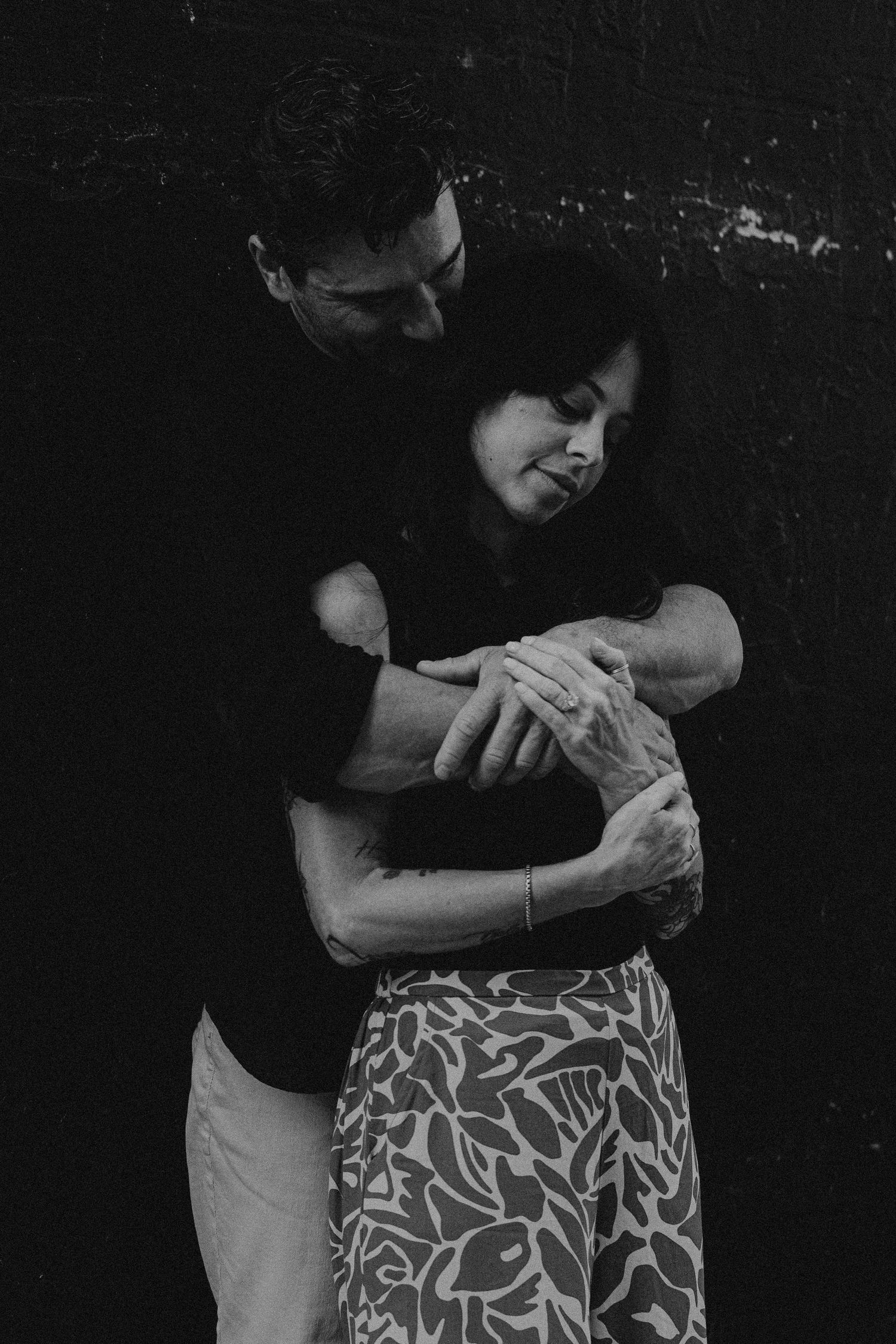 Black and white image of a couple embracing in front of a dark wall in Fort Lauderdale, Florida.