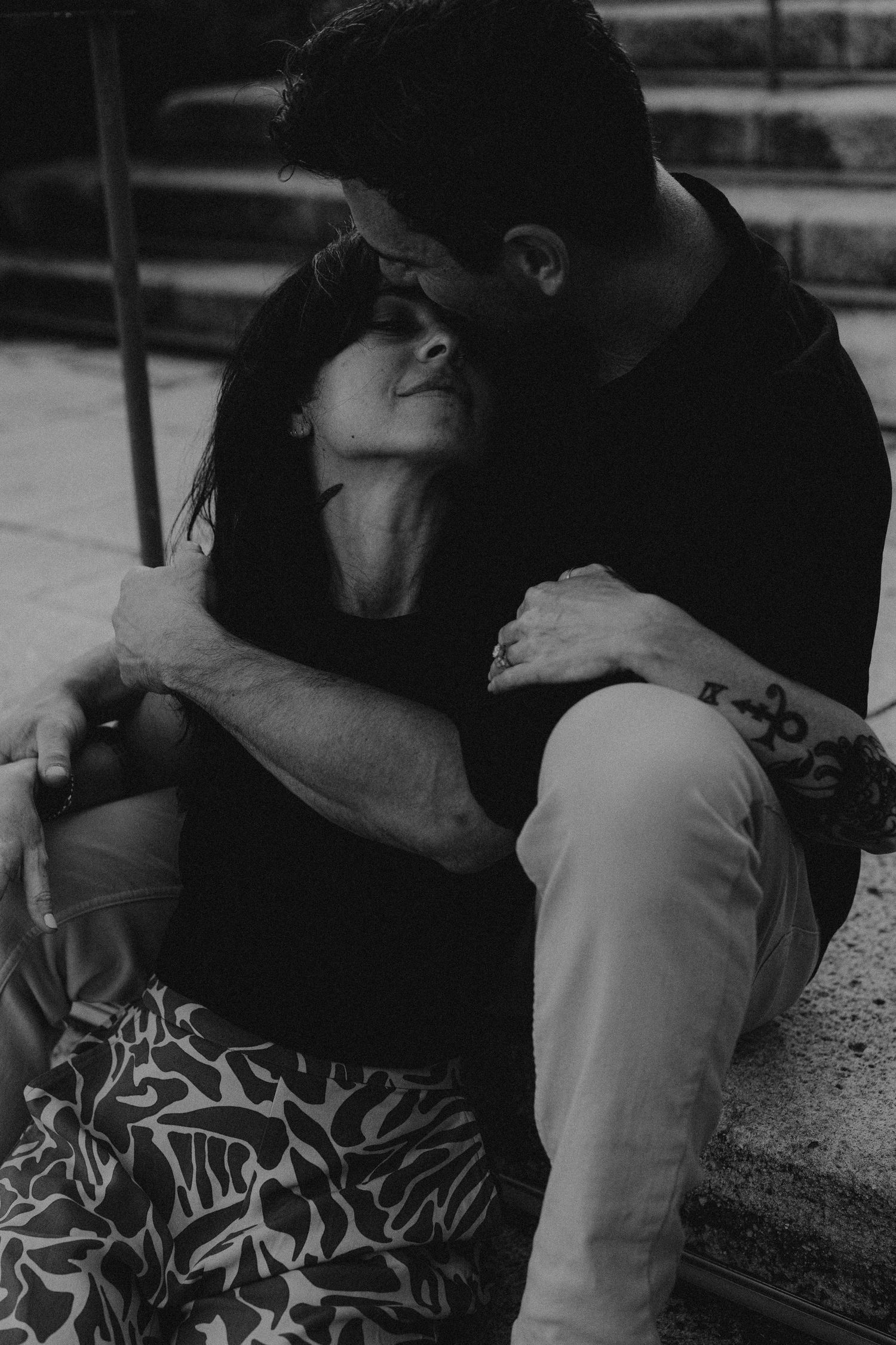 A romantic black and white photograph of an intimate couple sharing a tender moment on steps outdoors.