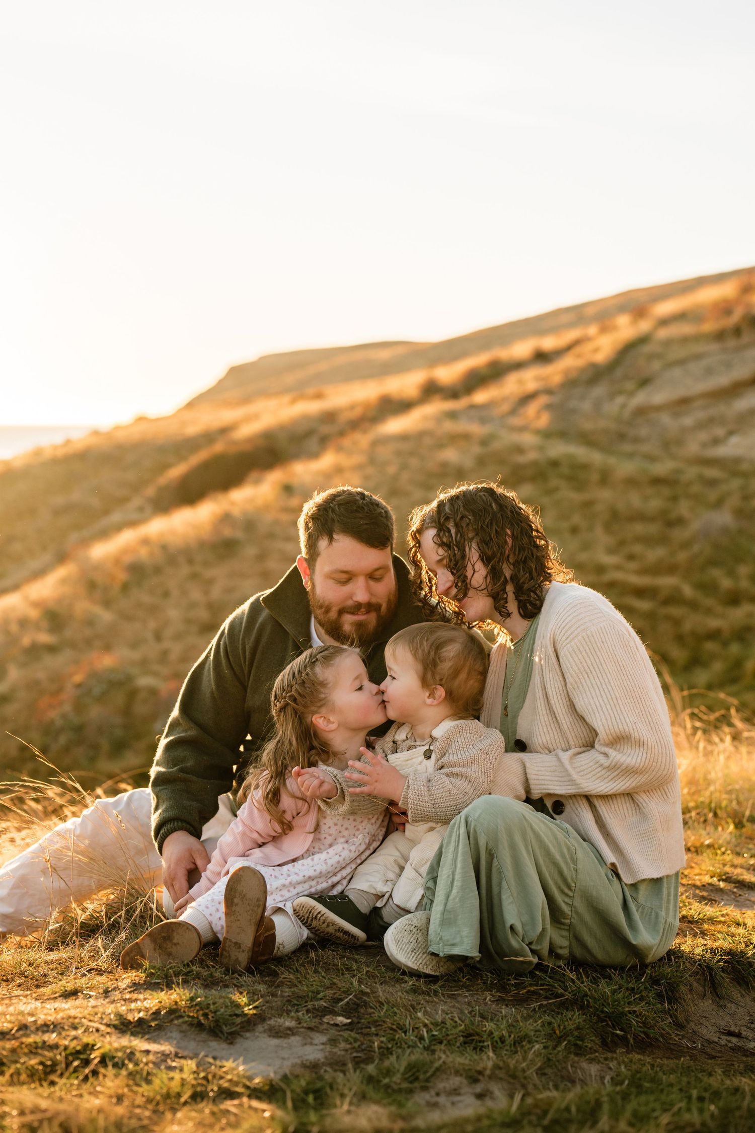 Family cuddling together in long grass during a relaxed outdoor family photography session in Christchurch
