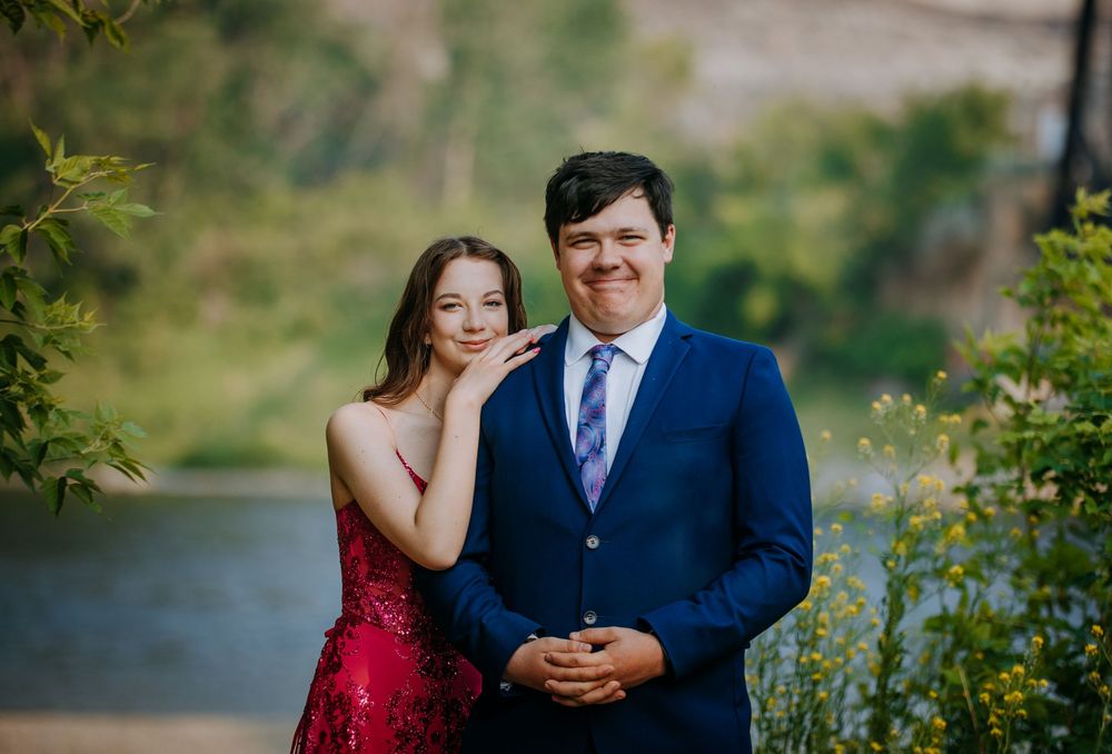 A man and a woman dressed formally stand together in a garden setting.