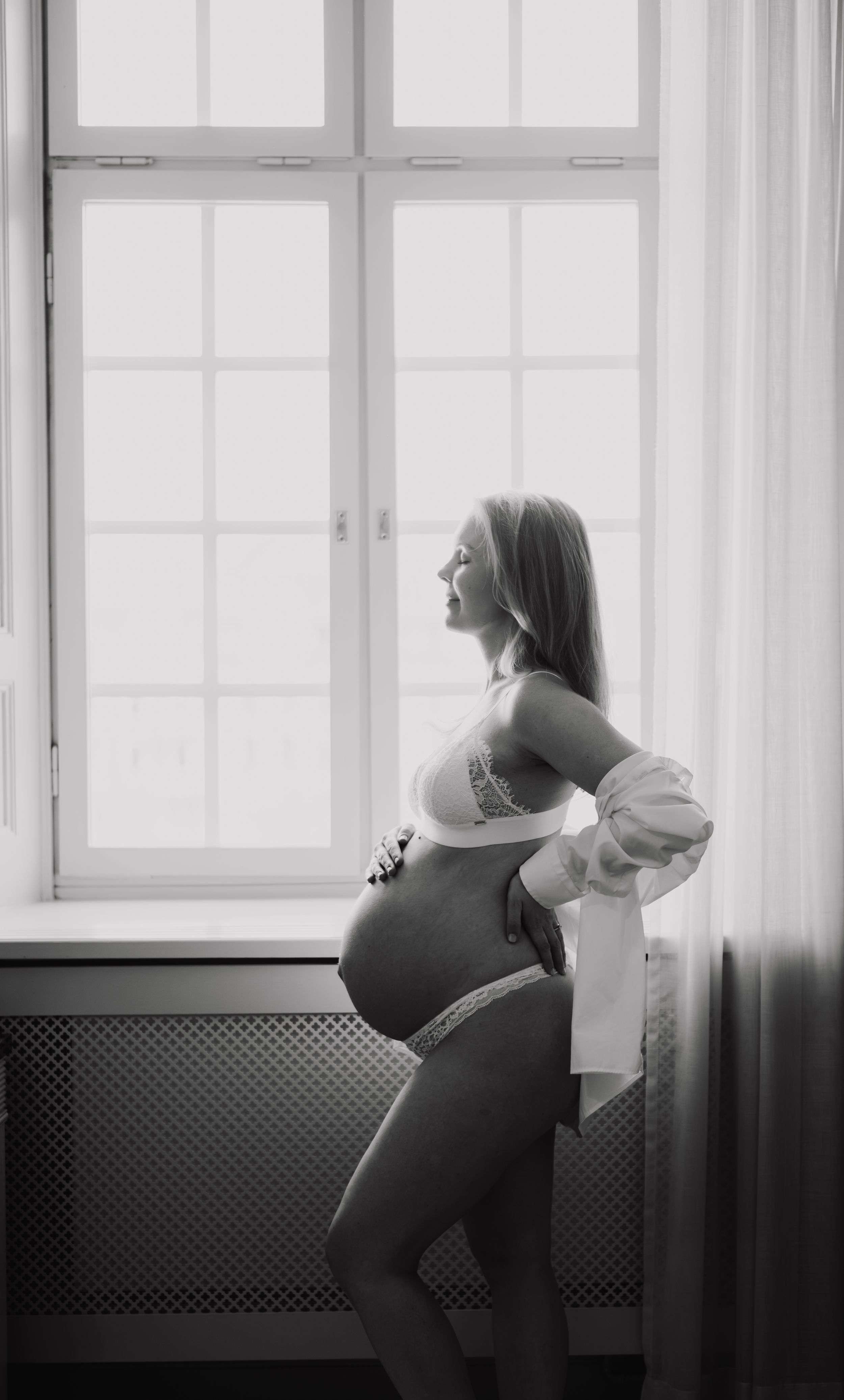 Avklädd gravid kvinna vid ett fönster