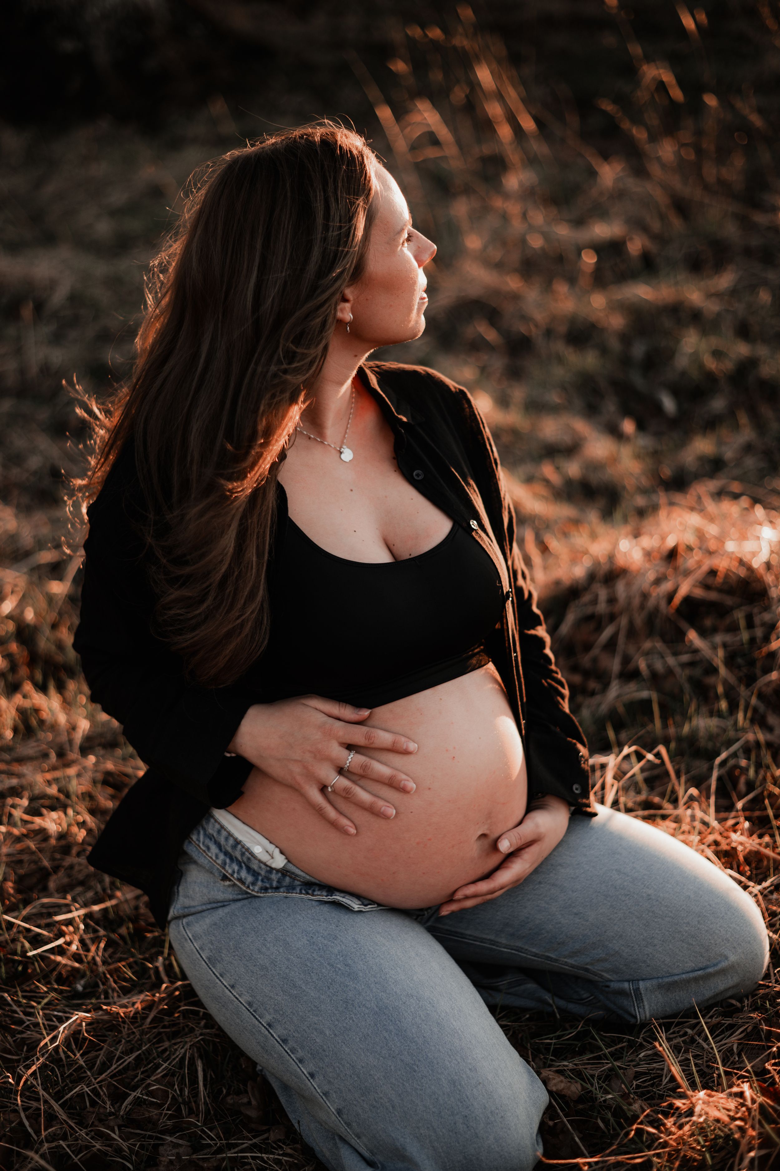 Gravid med uppknäppta jeans sitter på en äng