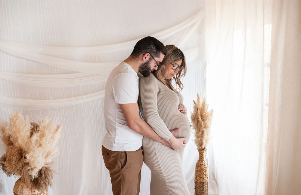 Couple attendant un enfant posant dans un décor studio bohème, séance maternité chaleureuse par votre photographe à Niort.