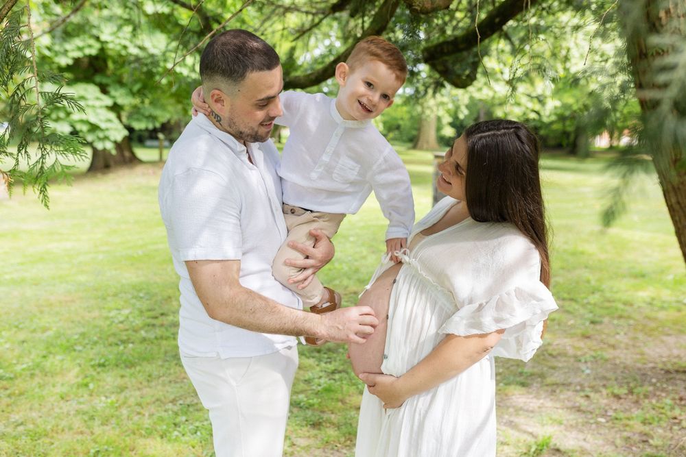 Famille s'enlaçant avec tendresse et l'aîné caressant le ventre rond, séance photo grossesse et famille pleine d'émotion à Niort, Frontenay.