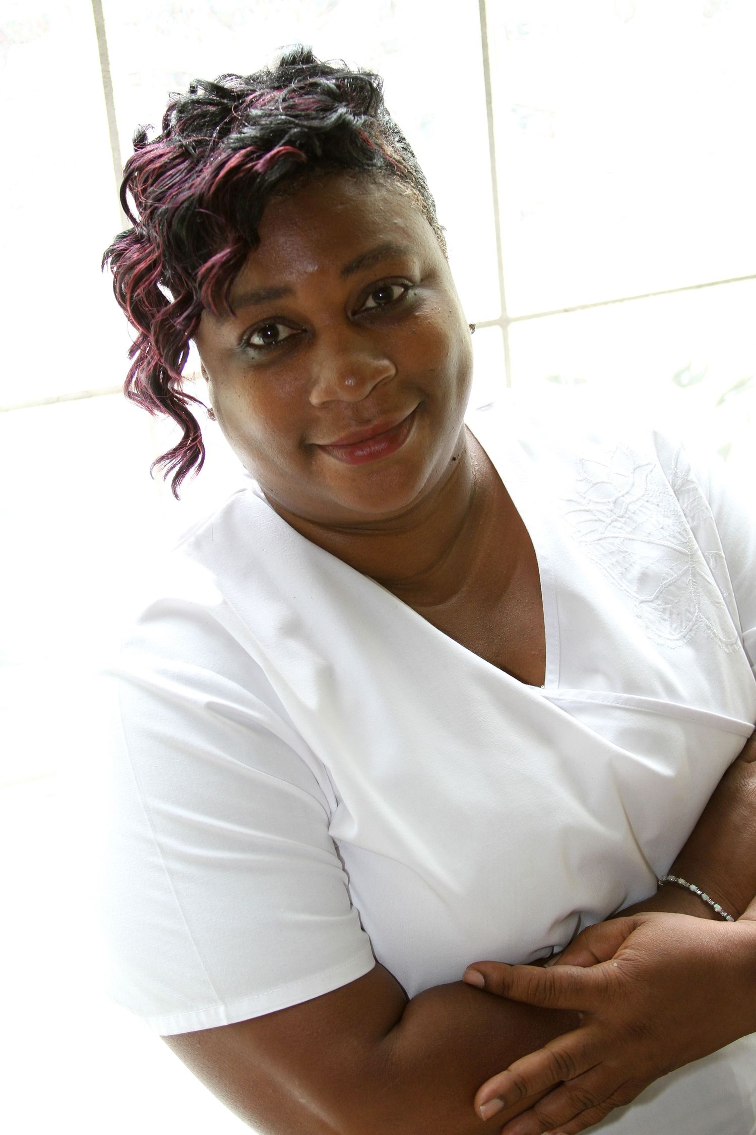 Portrait in white top with styled purple-tinted hair against light background.