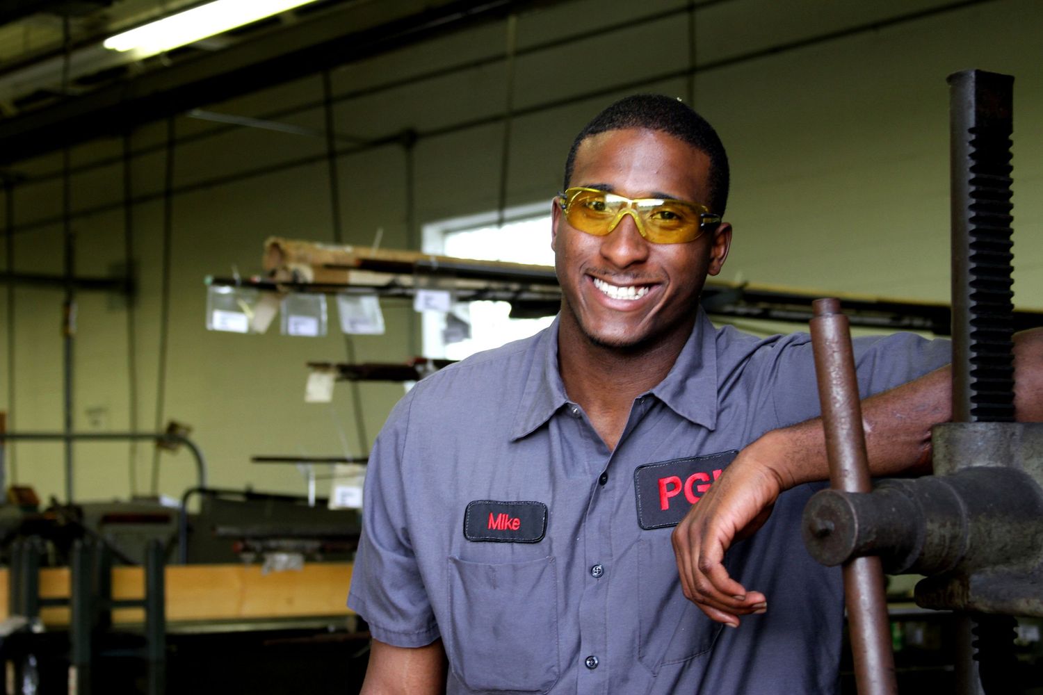 Smiling industrial worker in safety gear posing next to machinery in factory setting.