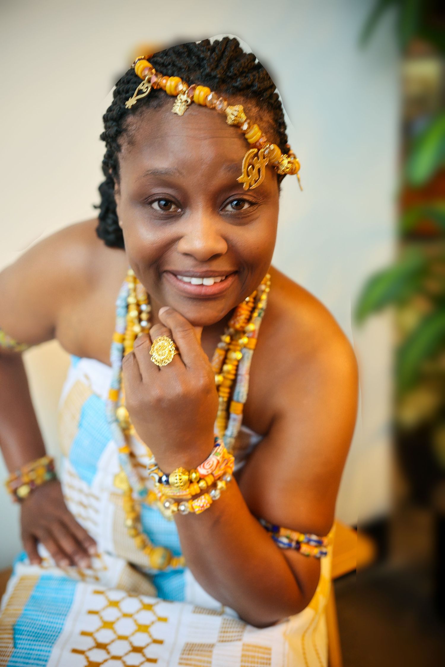 Traditional African-inspired fashion portrait featuring vibrant gold jewelry, beads and a blue patterned dress.