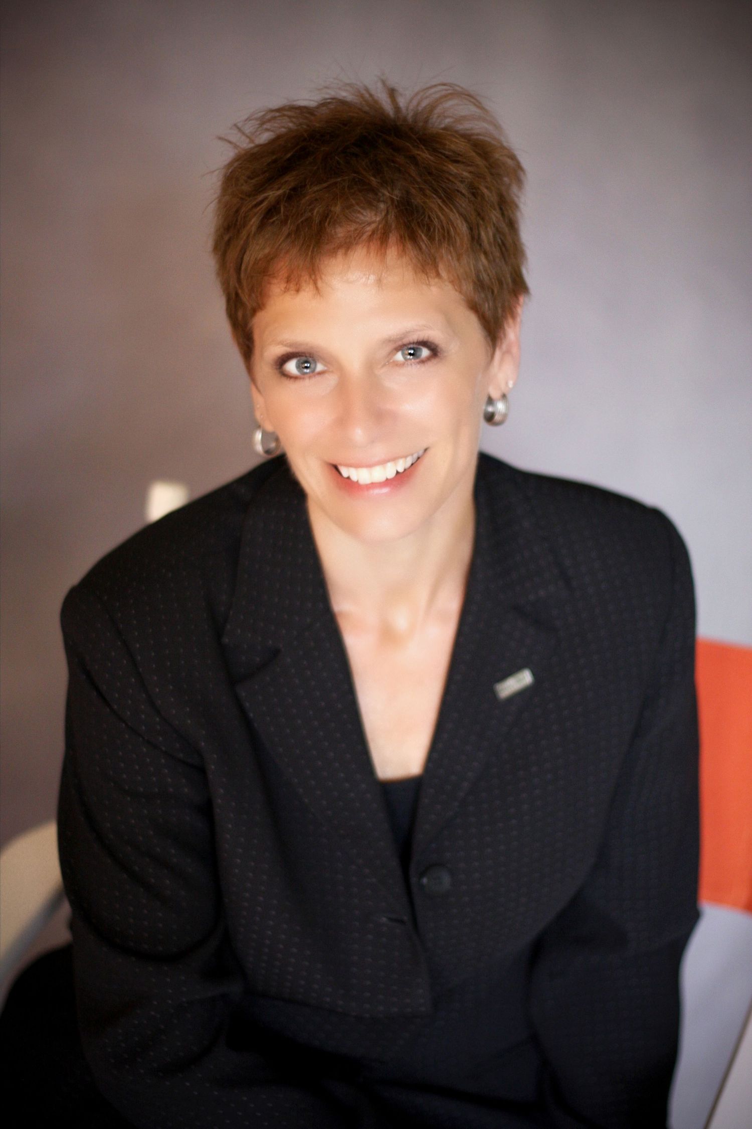 Professional business portrait of person in black blazer against neutral background.