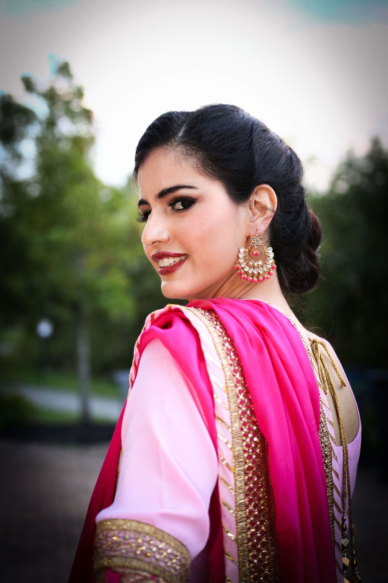 Portrait in traditional South Asian attire featuring bright pink dupatta and ornate jewelry.