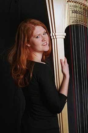 Musician poses with elegant wooden concert harp against dark background.