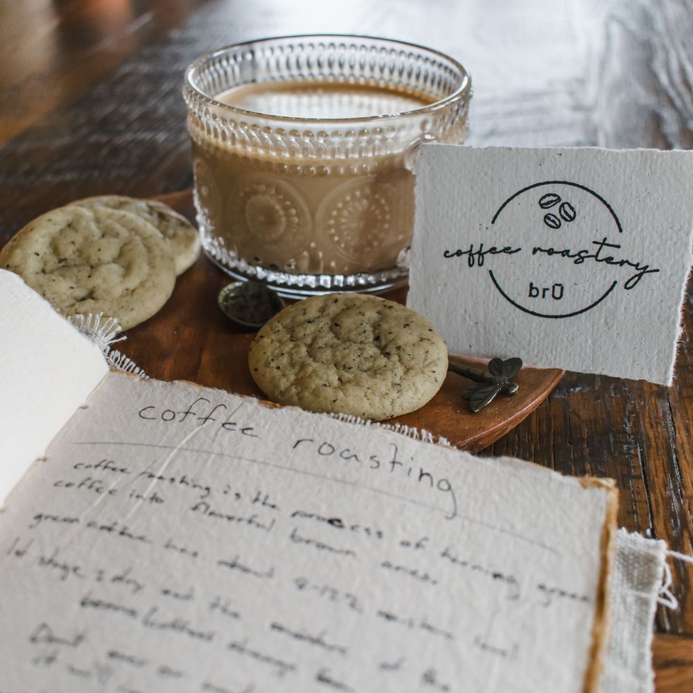 A glass of creamy coffee sits beside handwritten recipe notes and journal pages on a rustic wooden surface.