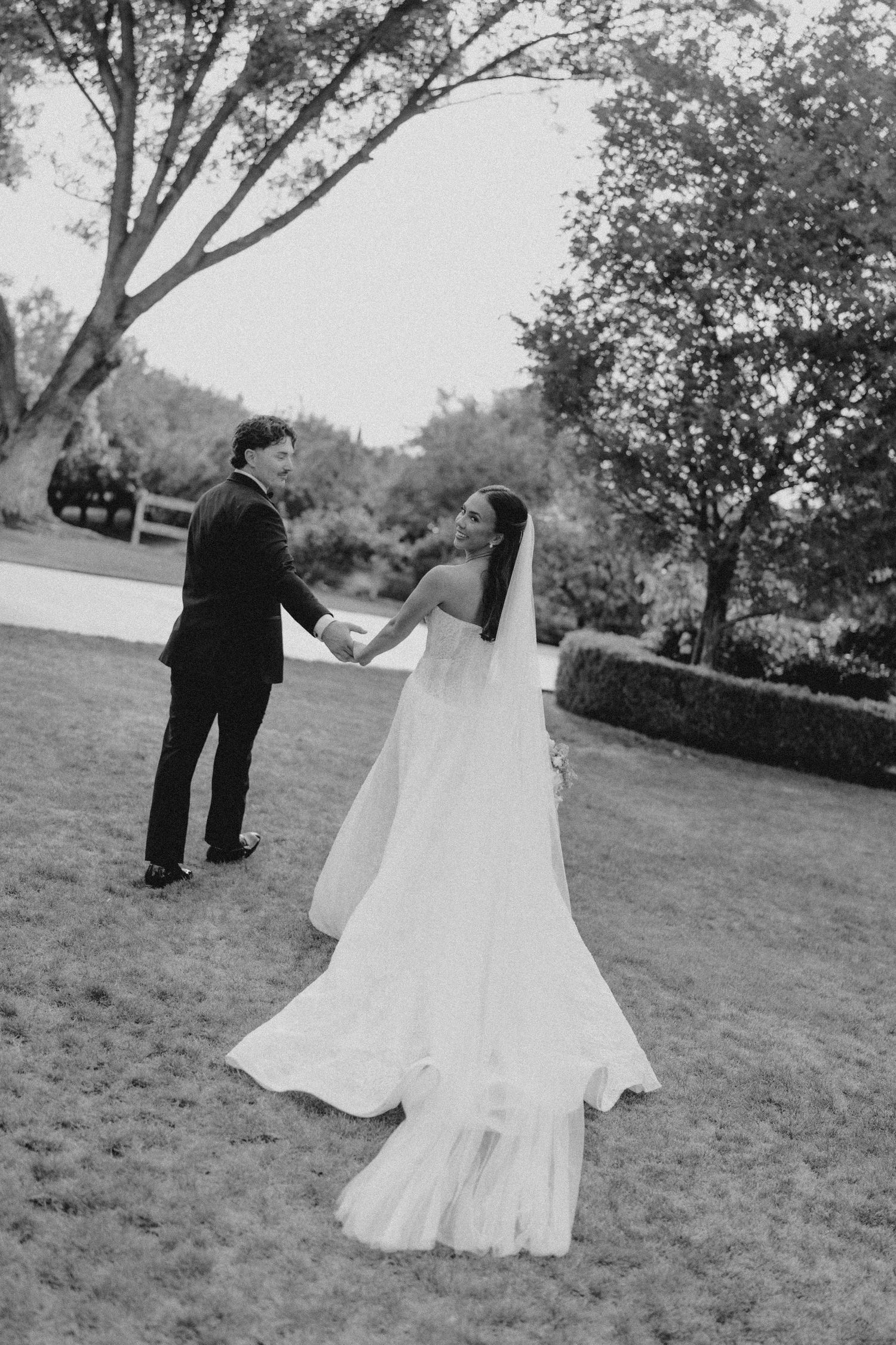 Fresno Wedding Videographer Packages. Black and white photo of a bride and groom holding hands on a lawn.
