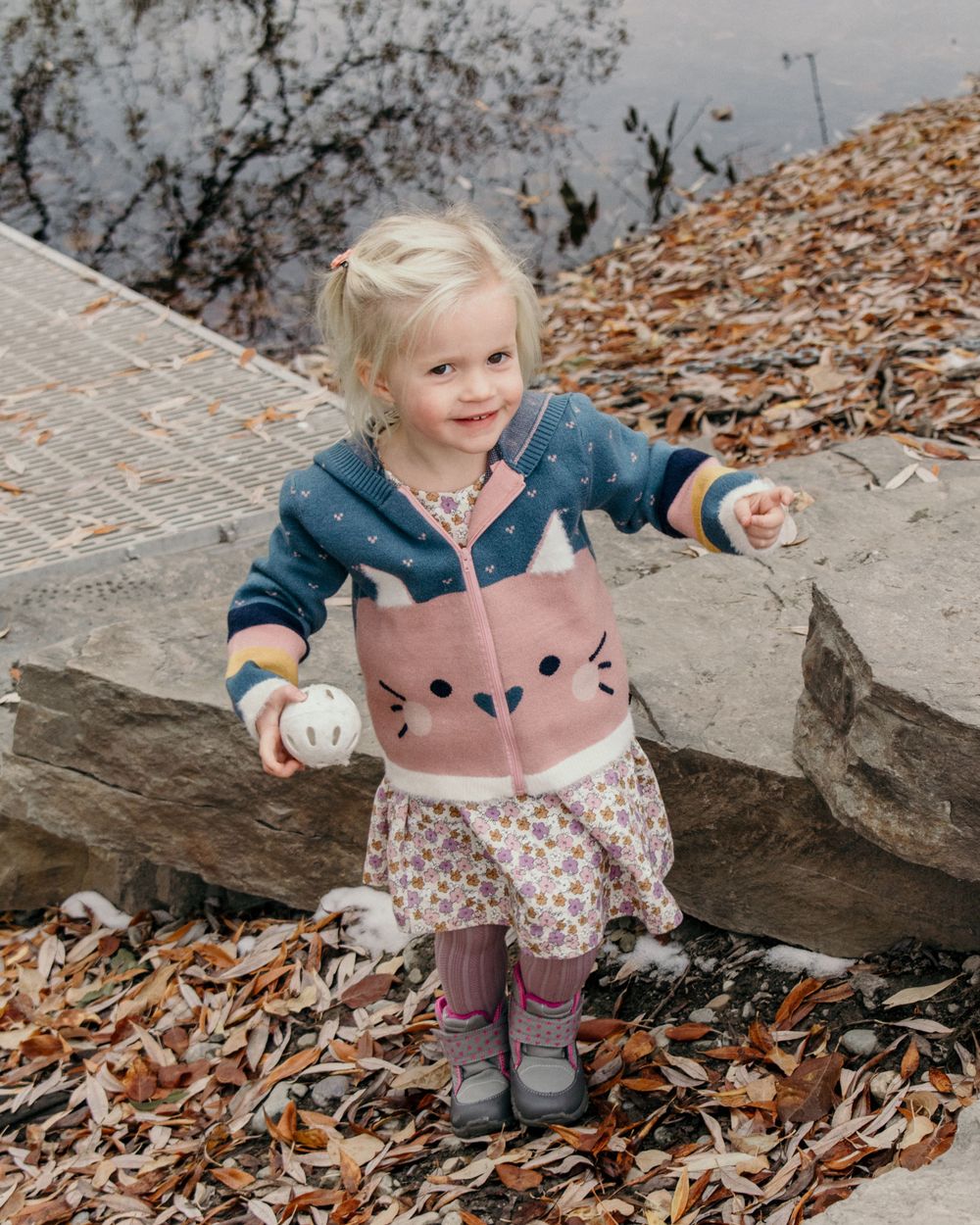 Toddler in a cute pink cat sweater playing among fallen autumn leaves.
Family, small girl, toddler