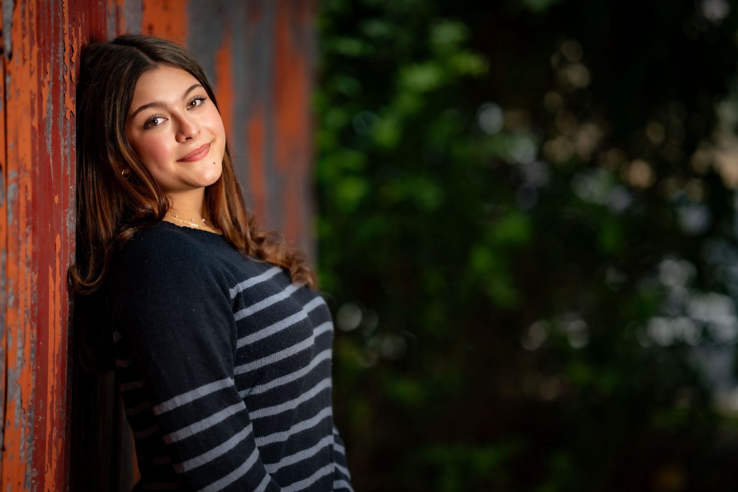 Portrait of person in striped sweater leaning against rustic wall outdoors.